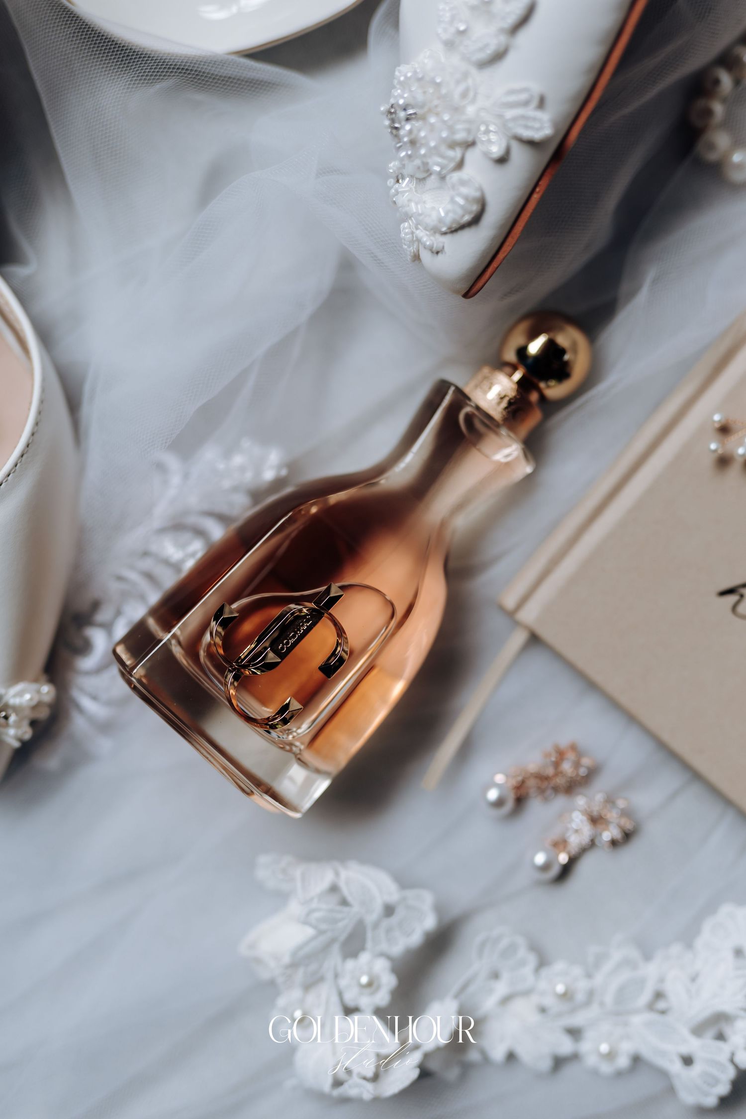 Wedding details with perfume bottles and delicate pearl accessories on white textured surface.