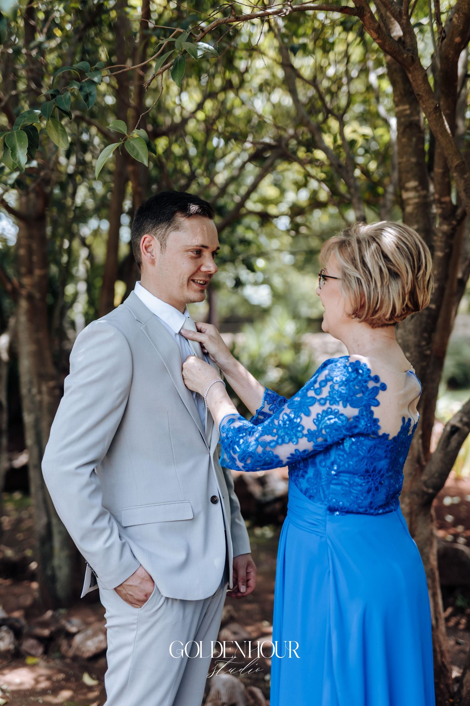 A tender moment outdoors with formal attire against a leafy green background.