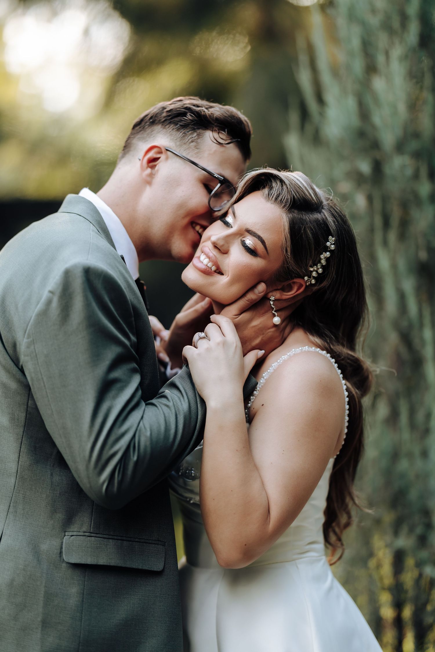 A tender wedding portrait captured outdoors with soft natural lighting and forest backdrop.