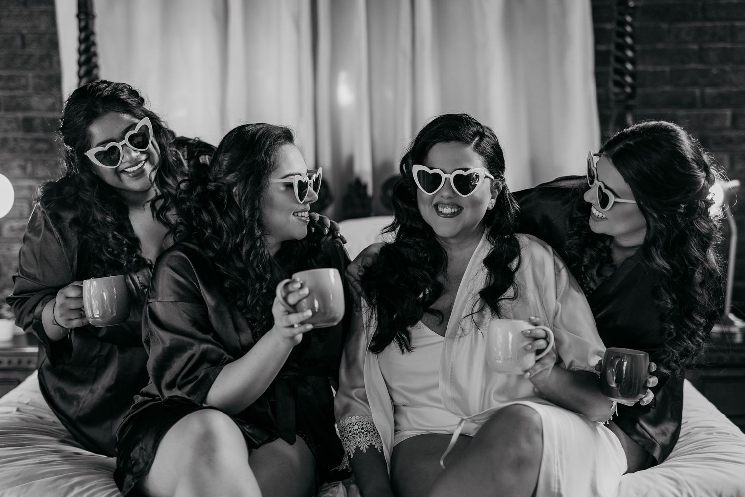 Wedding party members in black attire share candid moments while wearing retro sunglasses.