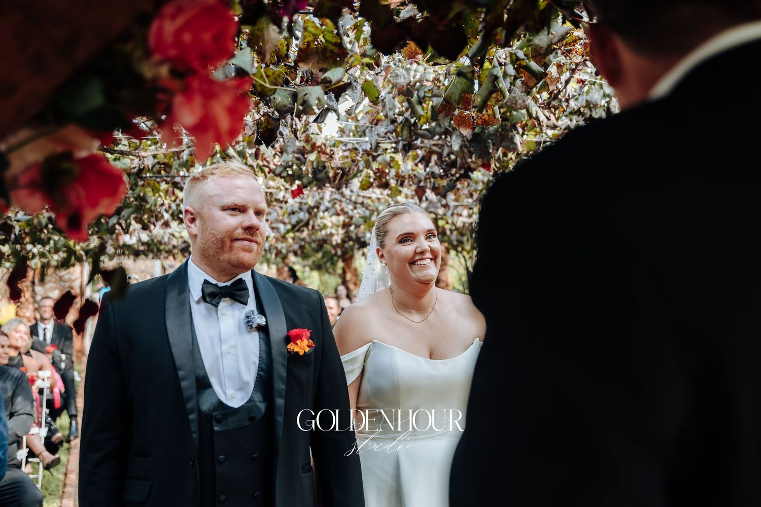 A romantic outdoor wedding ceremony under blooming cherry blossom trees with guests seated on white chairs.