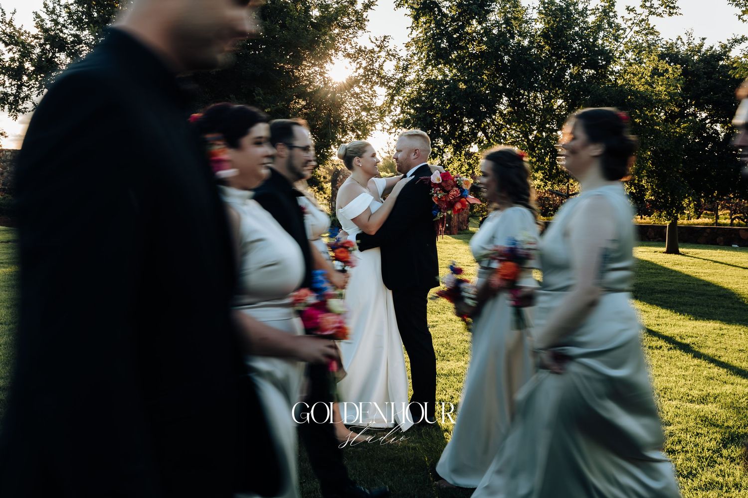 Wedding guests dance together outdoors during a golden sunset celebration in a grassy park setting.