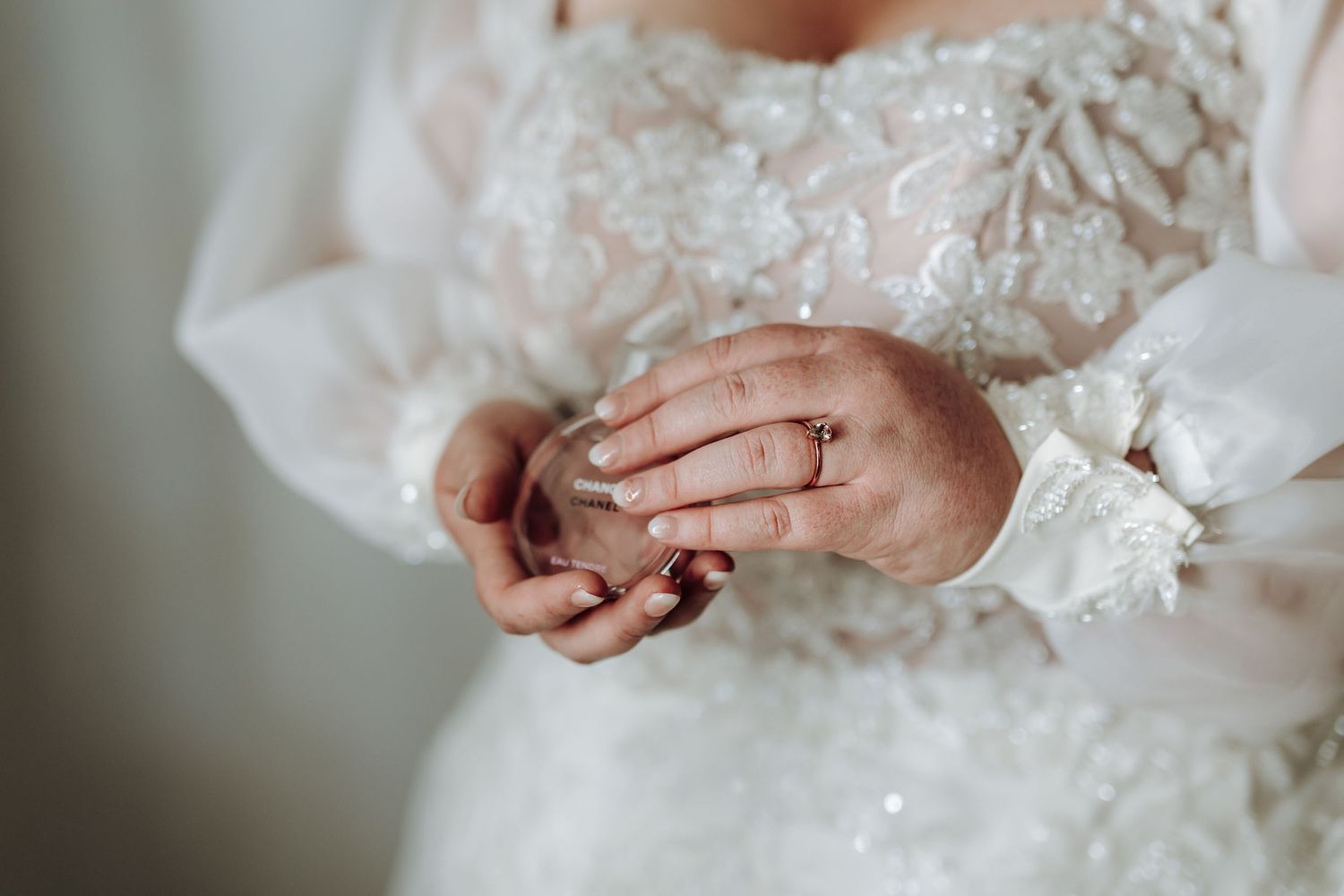 Close up details of delicate white lace and tulle on a wedding dress with hands gently touching the fabric.