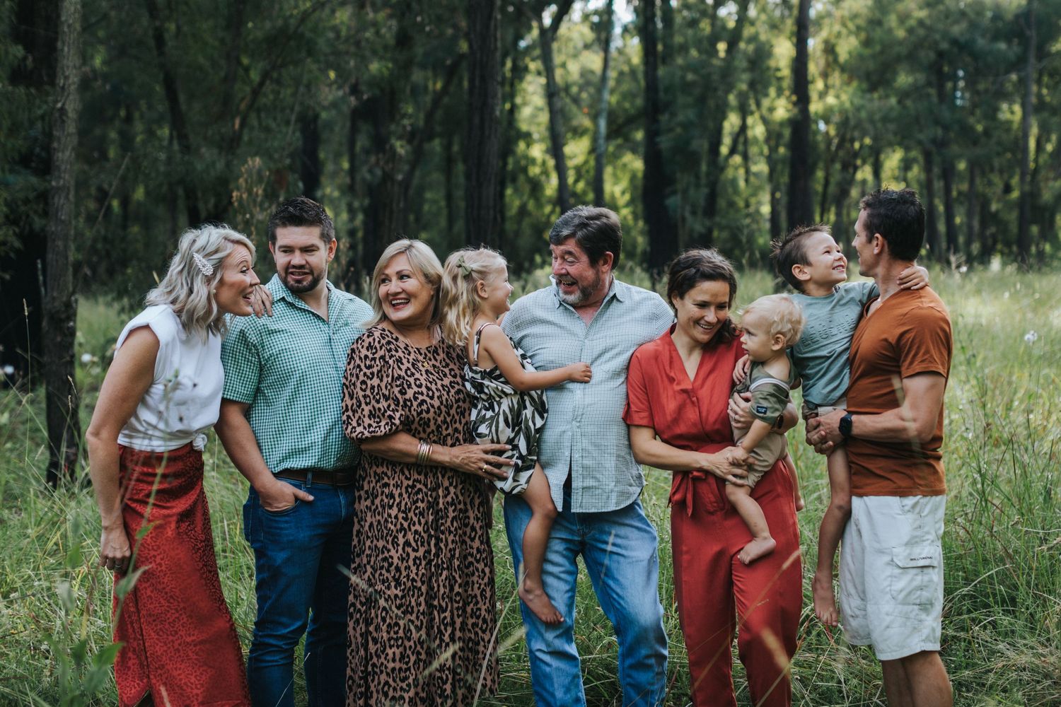 A series of candid family portrait photos taken outdoors in a sunlit wooded area with natural lighting and casual poses.