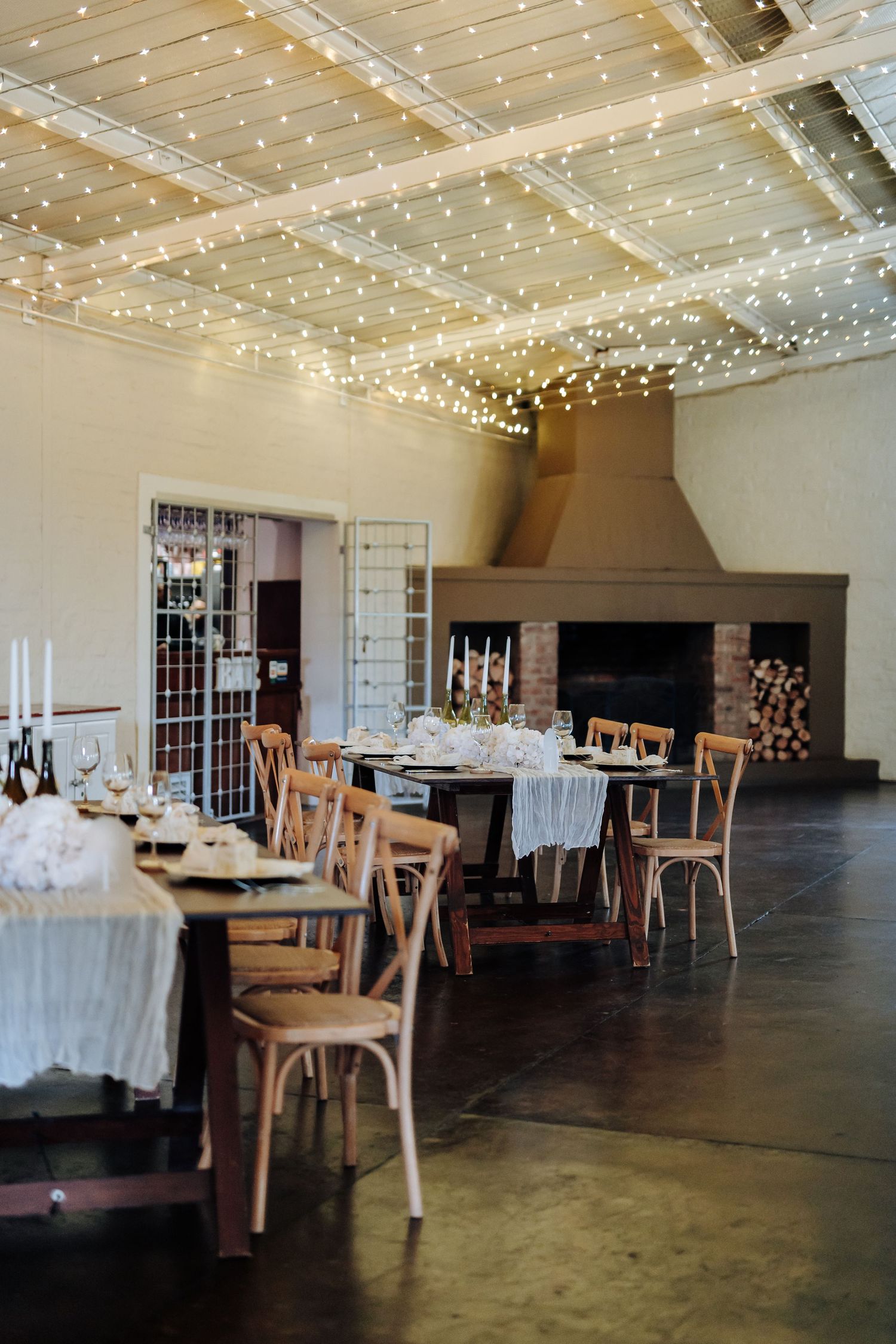 Rustic event venue interior with wooden chairs, concrete floors, and twinkling string lights decorating the ceiling.