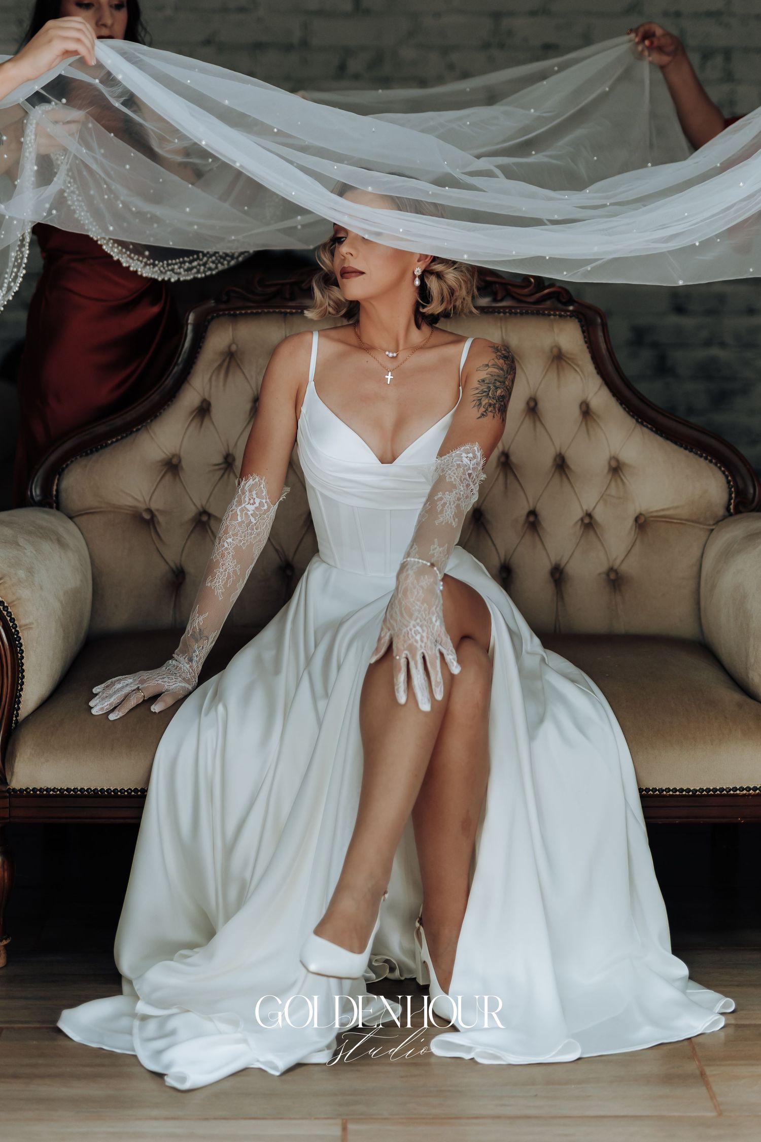 Elegant bridal details featuring flowing white dress and veil on tufted vintage sofa.