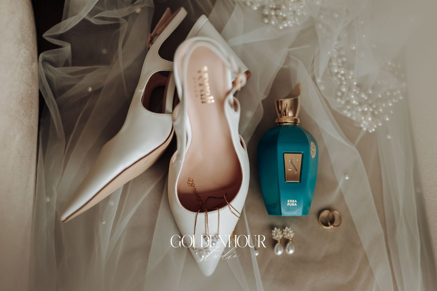 Wedding accessories including elegant white heels, perfume bottles, and jewelry arranged on a soft tulle background.