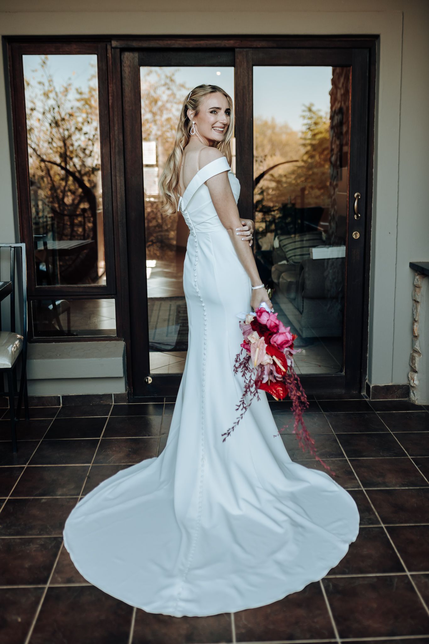 Full length shot of modern wedding dress with flowing train and bright red floral bouquet.
