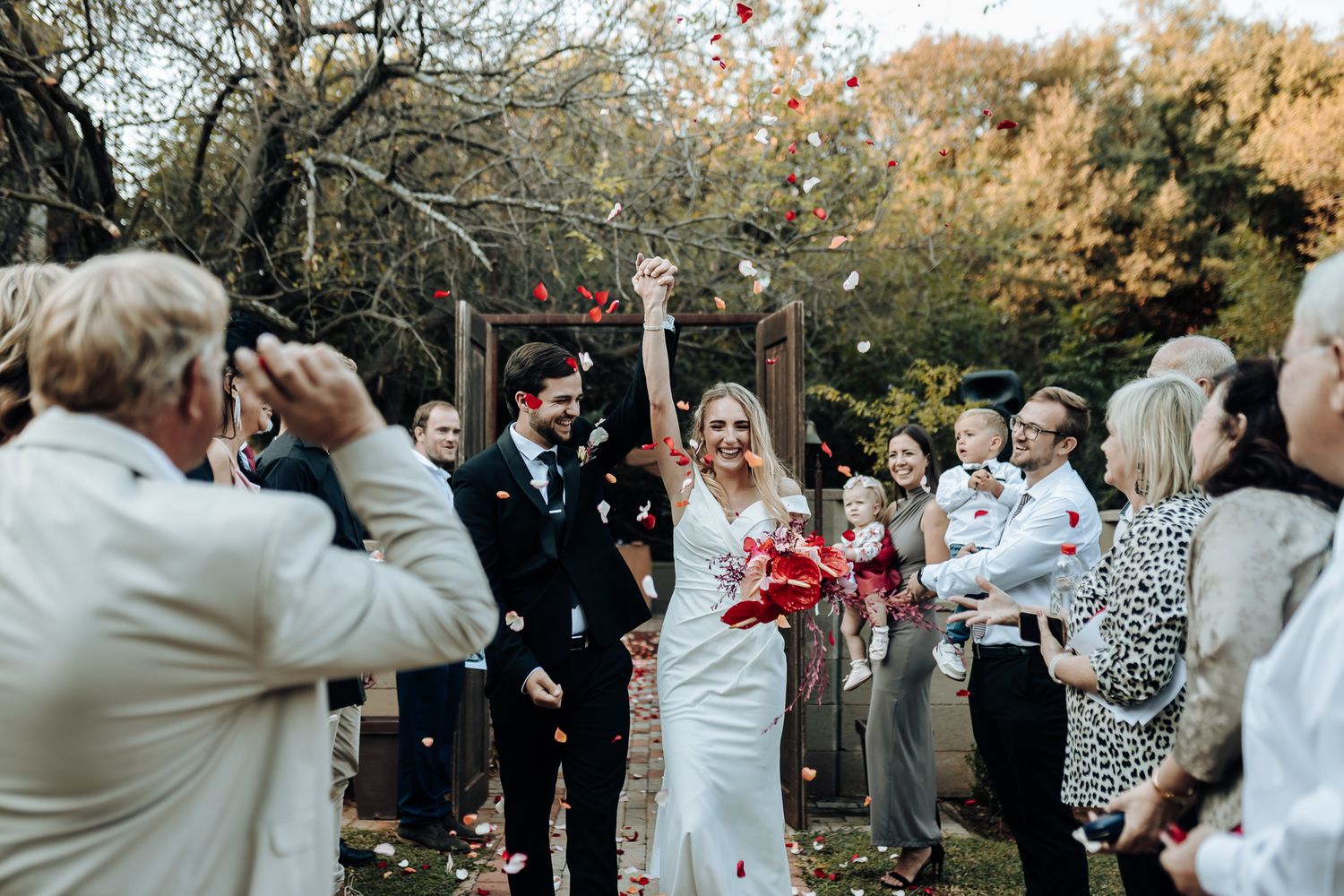 Wedding guests capture photos of celebrating newlyweds during autumn outdoor ceremony.