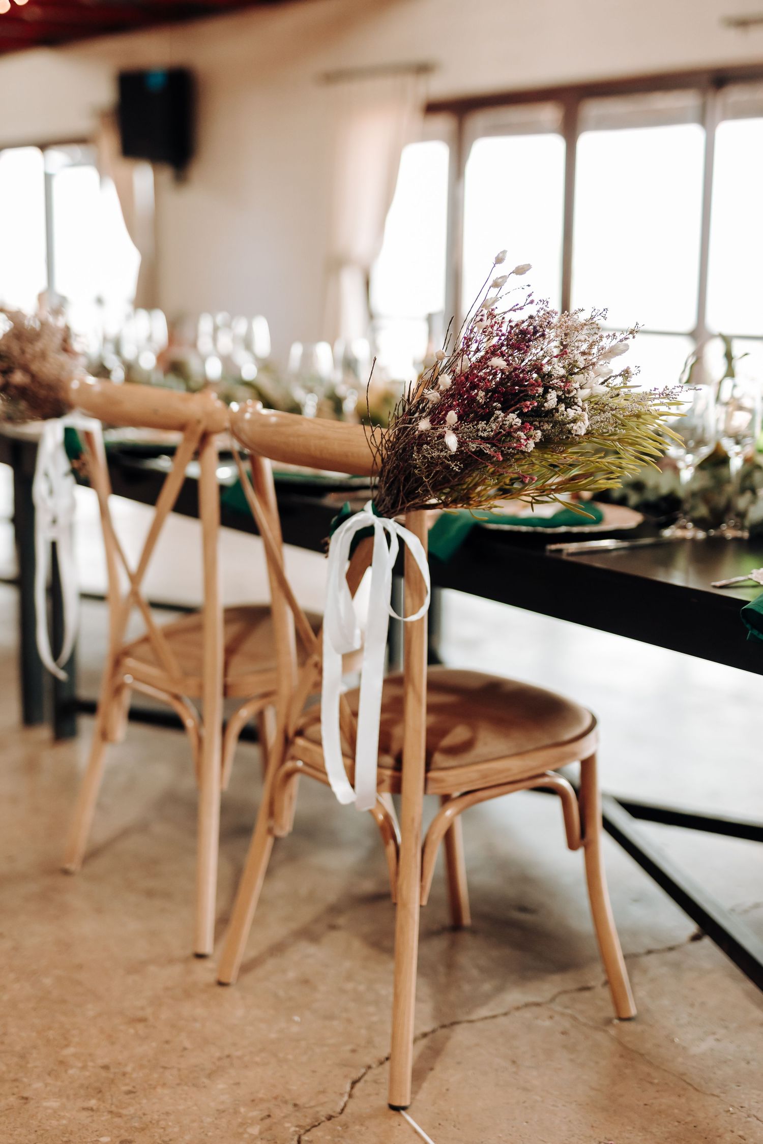 Rustic wooden chair decorated with dried flowers and white ribbon at a wedding reception.