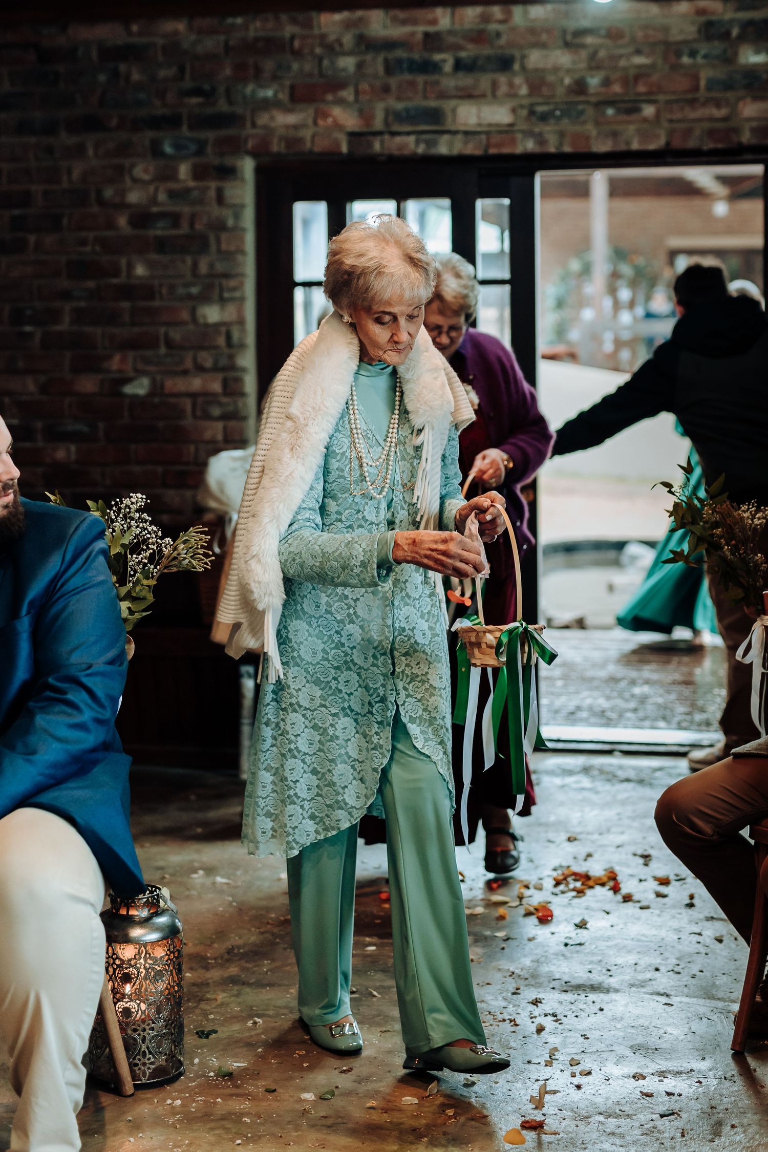 Two elegant attendees walking through a rustic brick venue wearing formal attire with vintage flair and accessories.