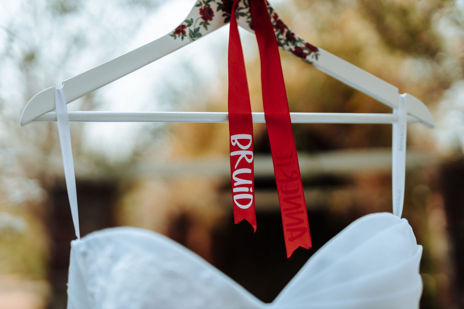 White wedding dress on hanger with red ribbon detail.
