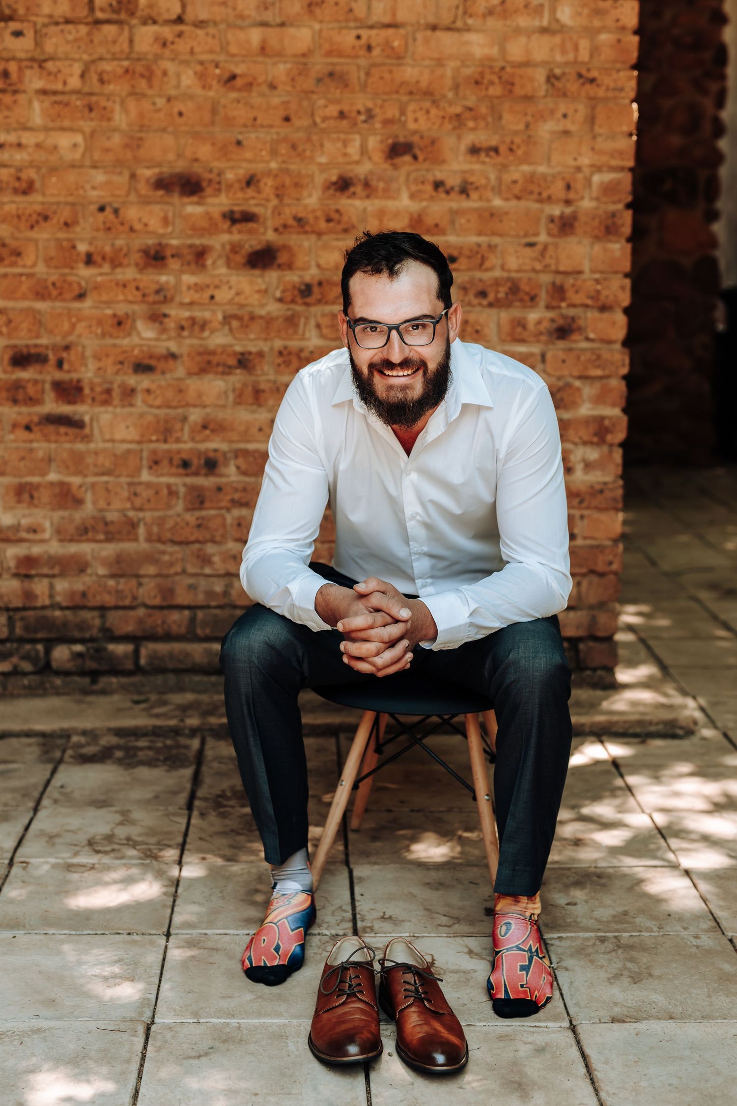 Portrait against brick wall featuring formal wear and casual footwear.