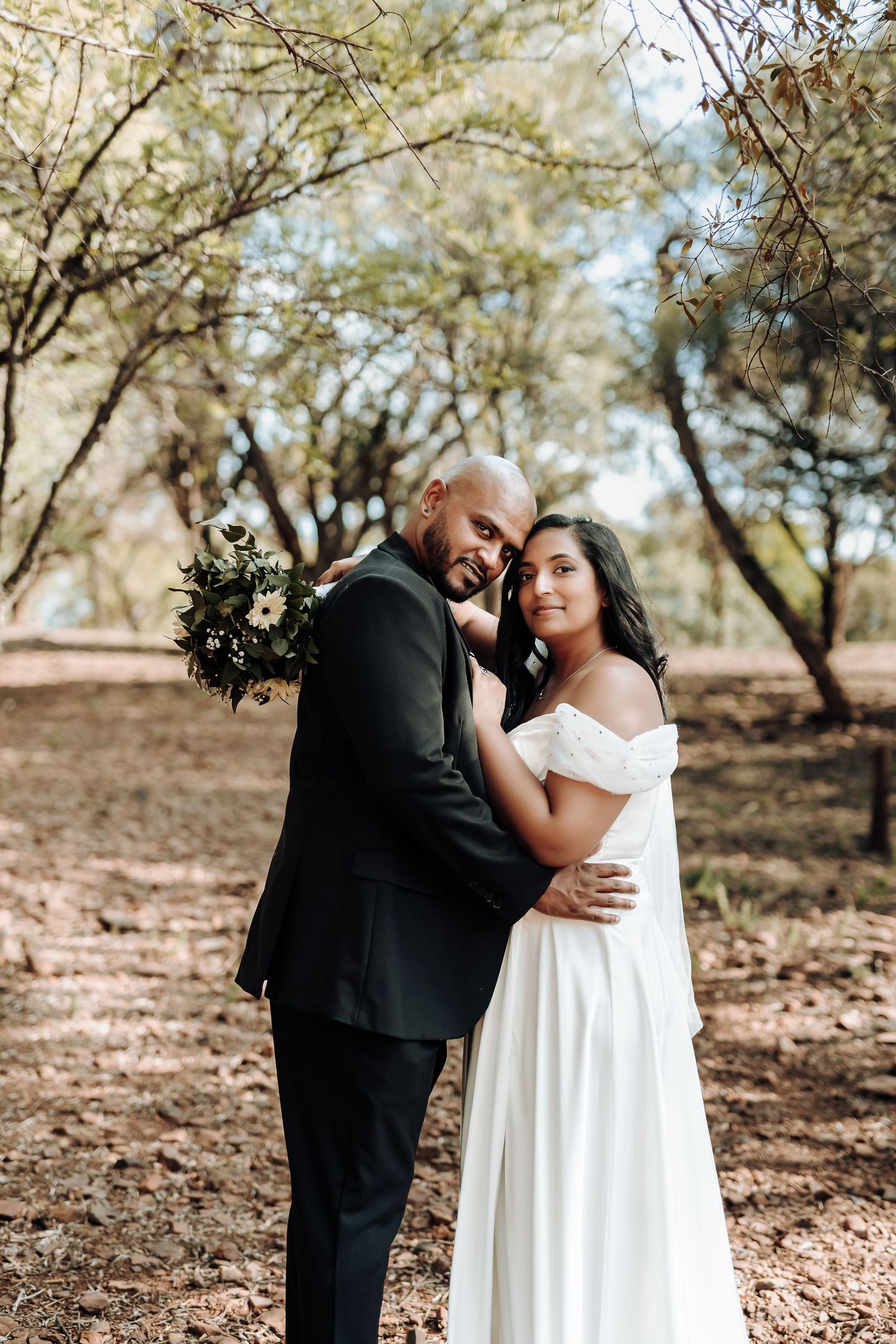 Romantic couple embrace during outdoor wedding photoshoot among trees.