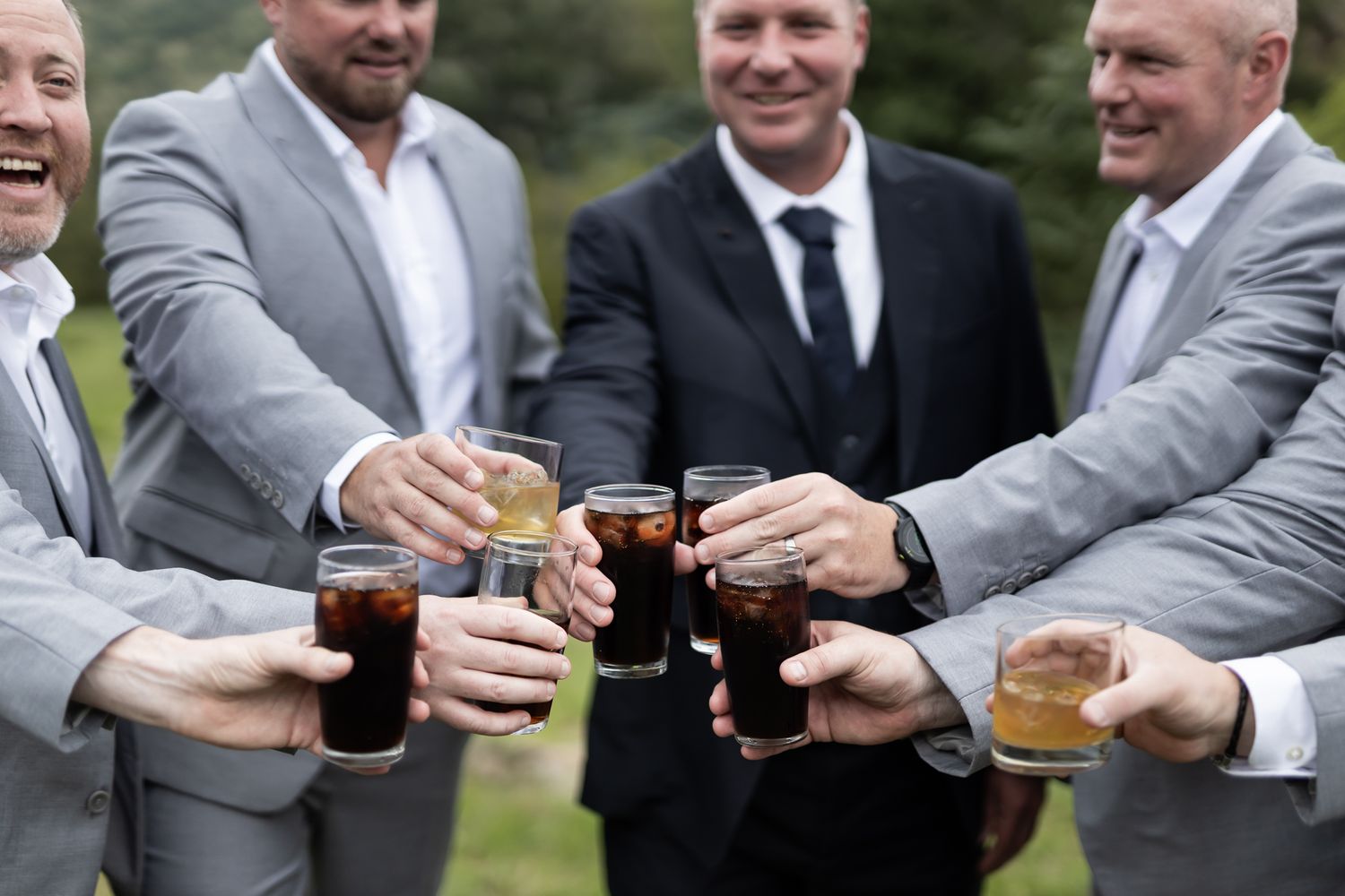 Groomsmen toasting with whiskey glasses in an outdoor celebration.