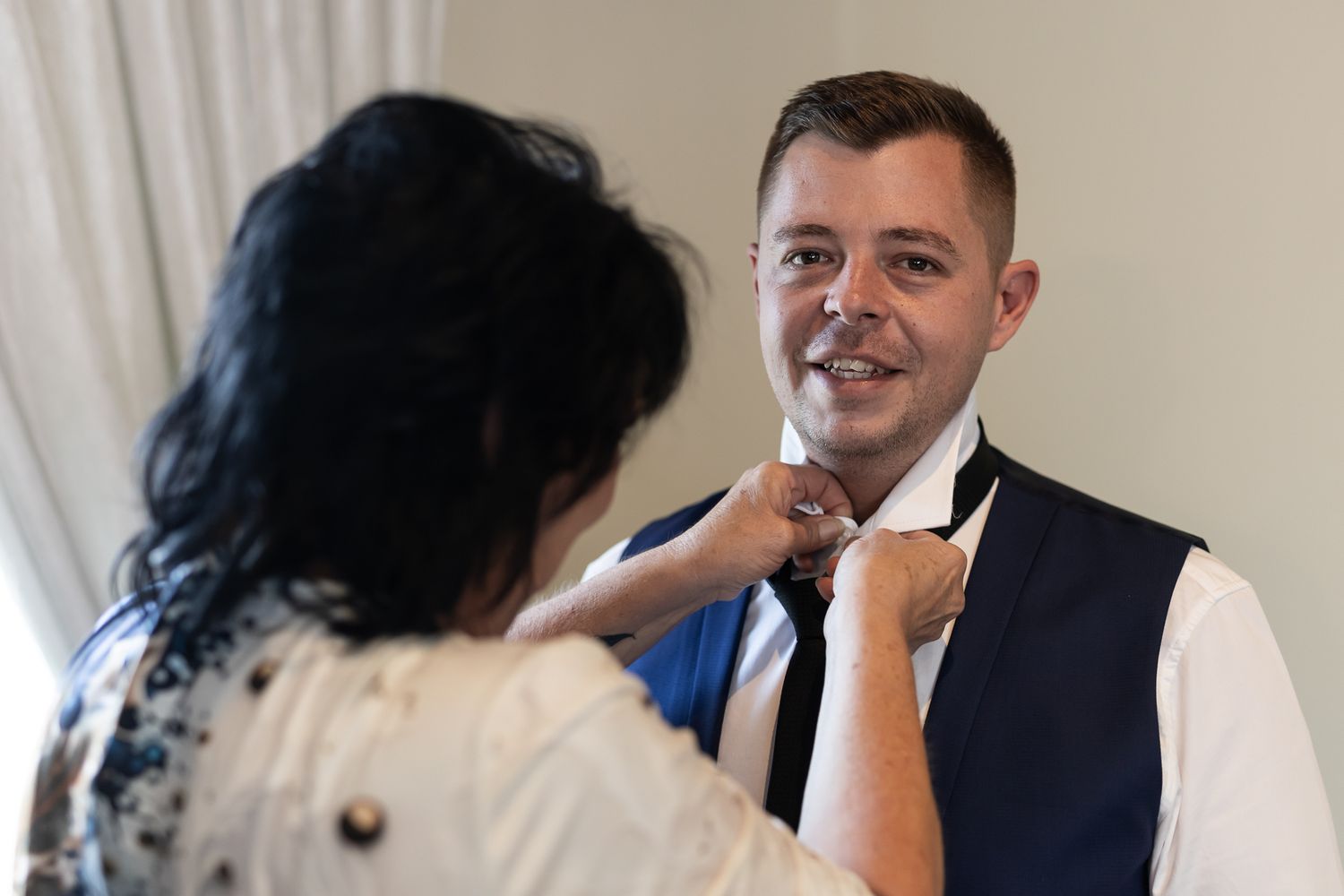 Someone adjusting a tie on formal attire during wedding preparations.