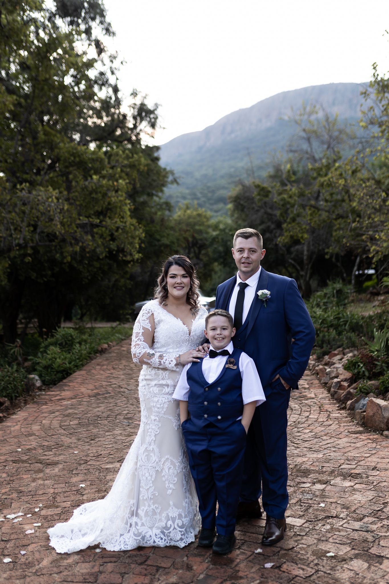 Wedding portrait of couple with young ring bearer on rustic mountain path.
