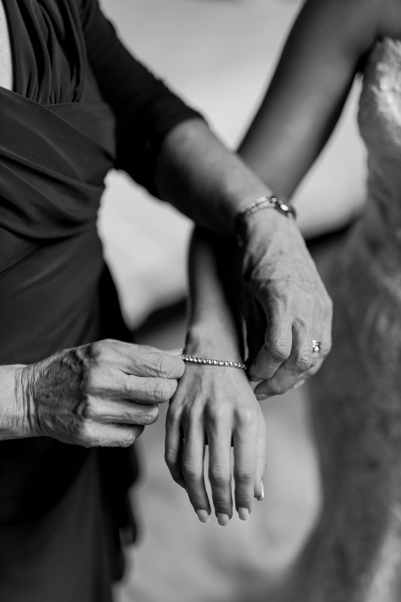 Black and white close-up of hands placing jewelry on wrist during wedding preparations.