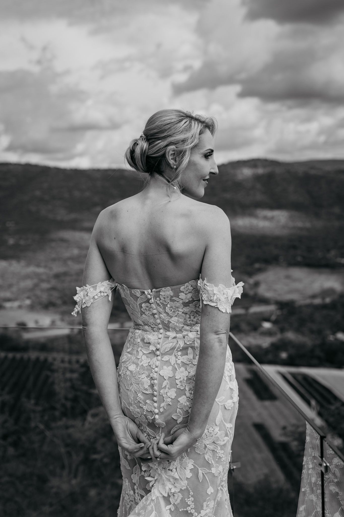 Black and white portrait of bride in lace gown overlooking mountain vista.