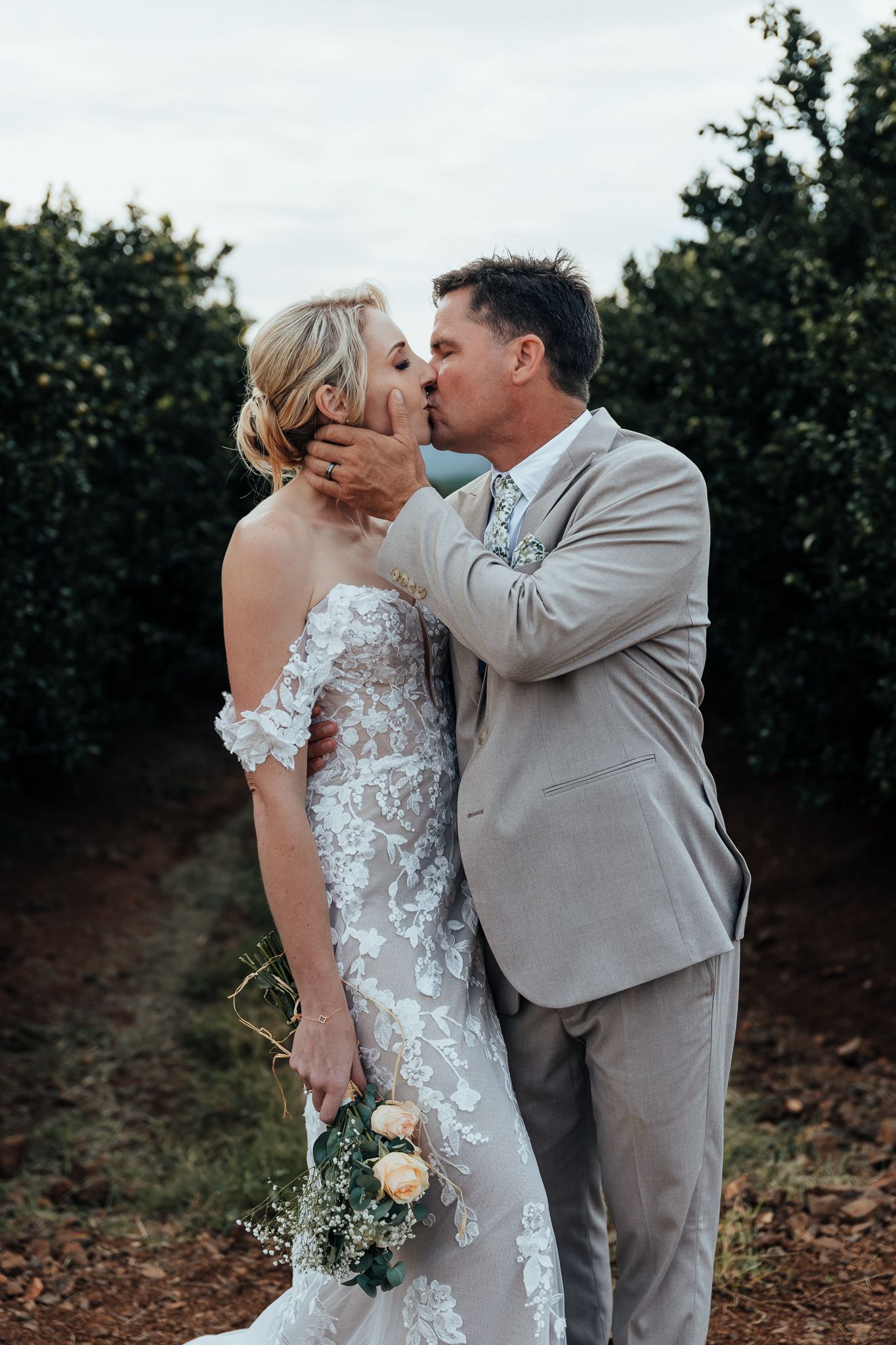 Romantic moment between newlyweds in an orchard setting with bride holding a bouquet.