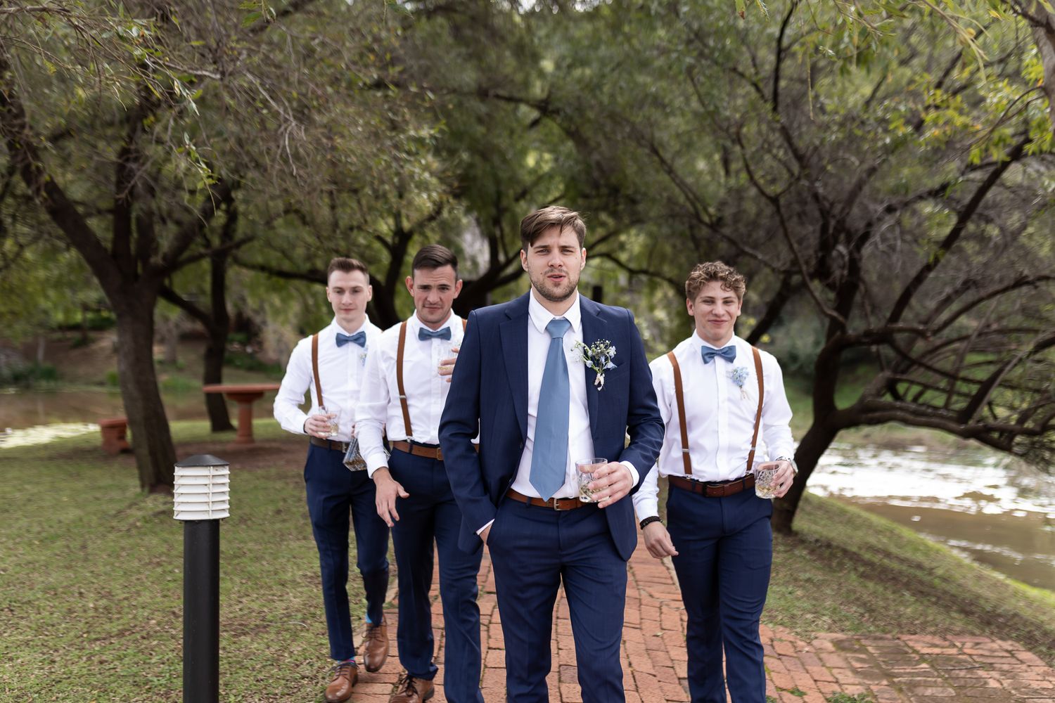 Wedding party in navy suits and suspenders posing outdoors in natural setting.