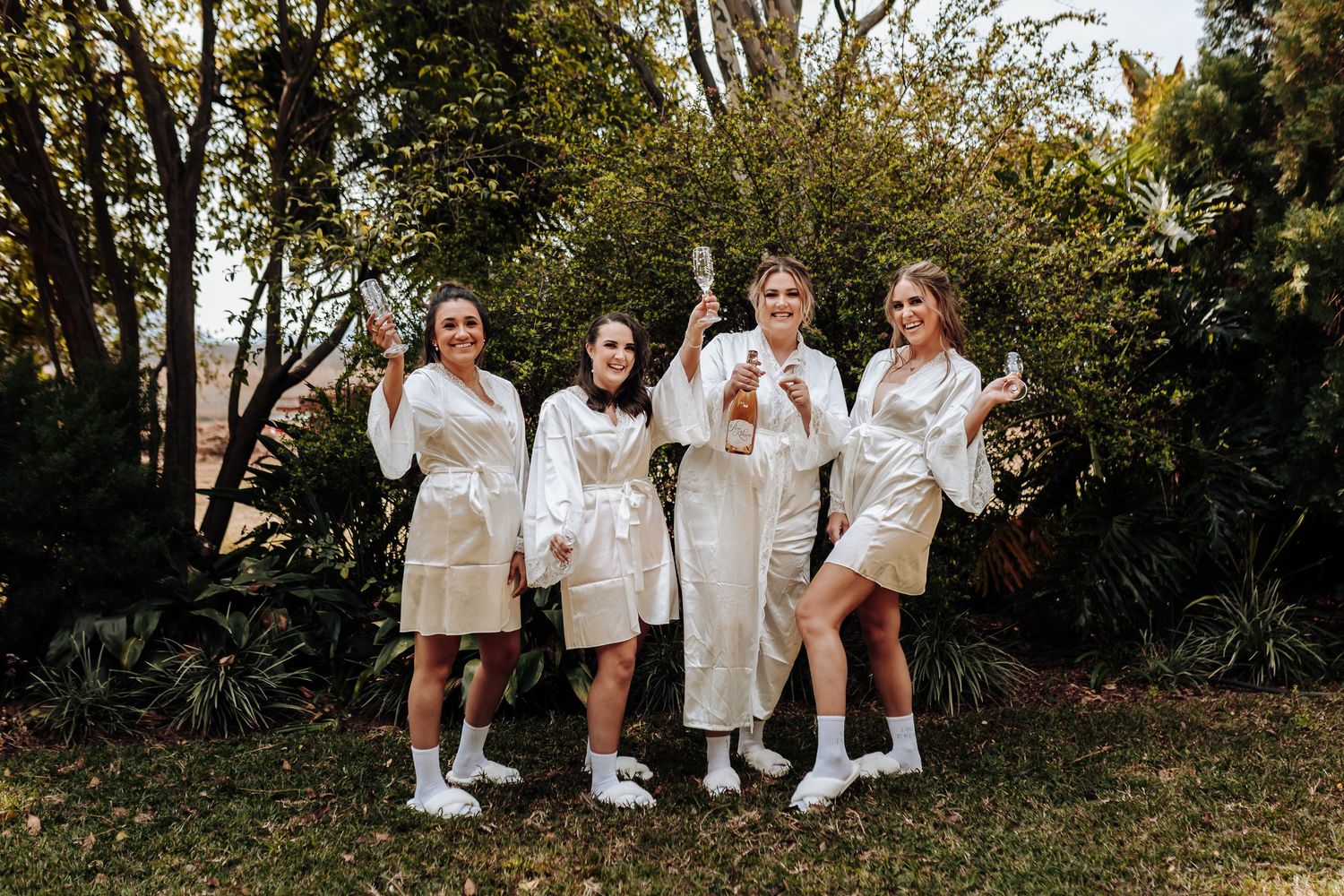 A group in matching white robes and sneakers pose together outdoors against a natural backdrop of trees and greenery.