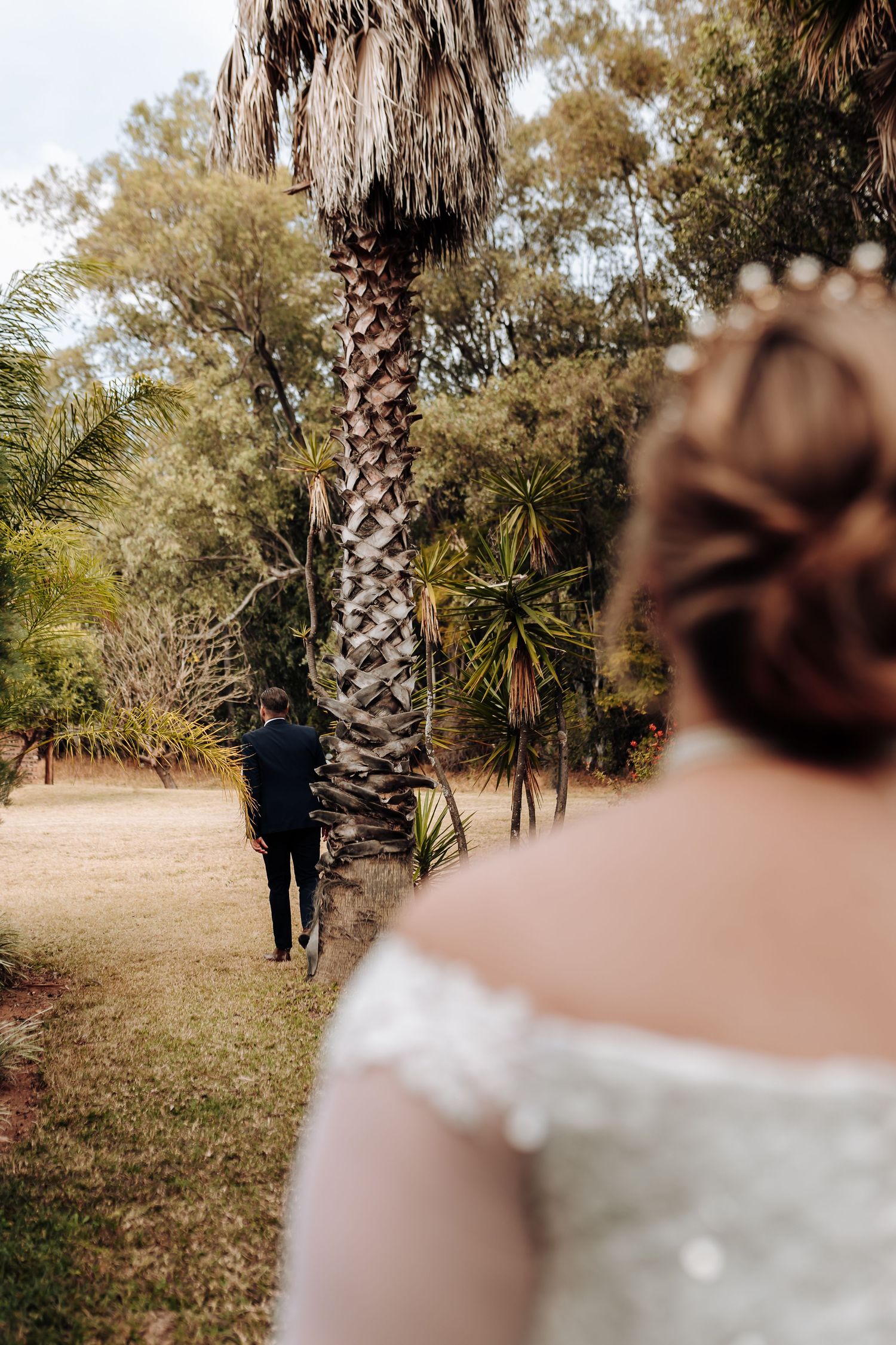 A couple shares a romantic first look moment in a garden setting with tall palm trees and natural scenery.