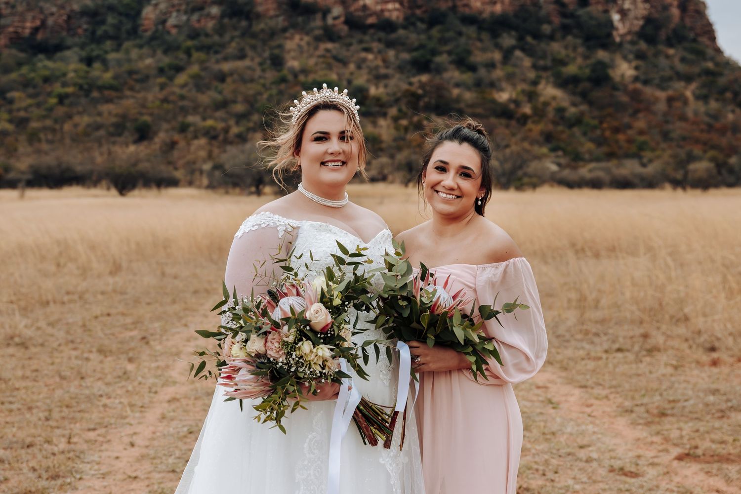Bridesmaids in blush pink dresses holding bouquets in a rustic outdoor setting.