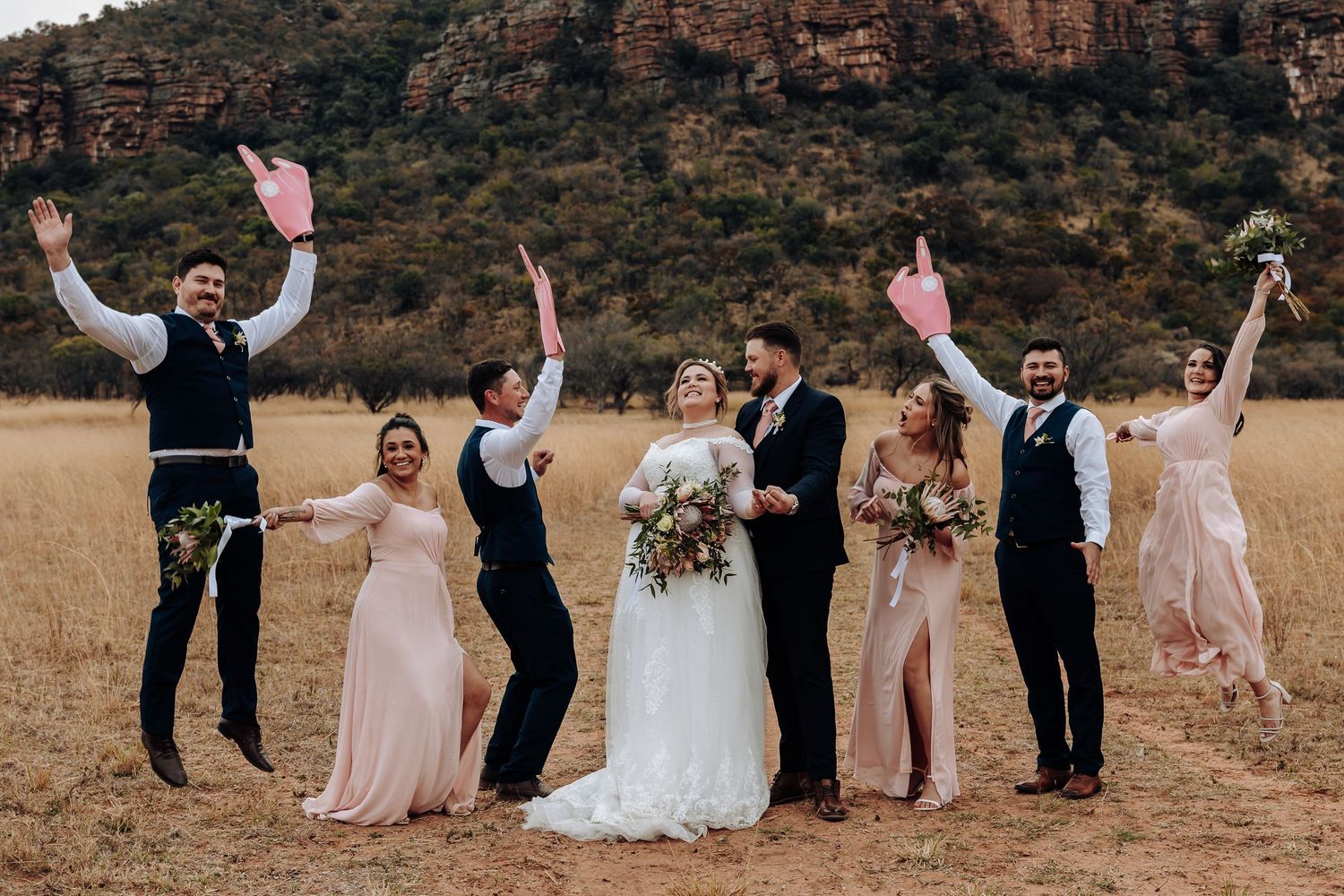Wedding party celebrates joyfully in front of scenic mountain backdrop at rustic outdoor ceremony.