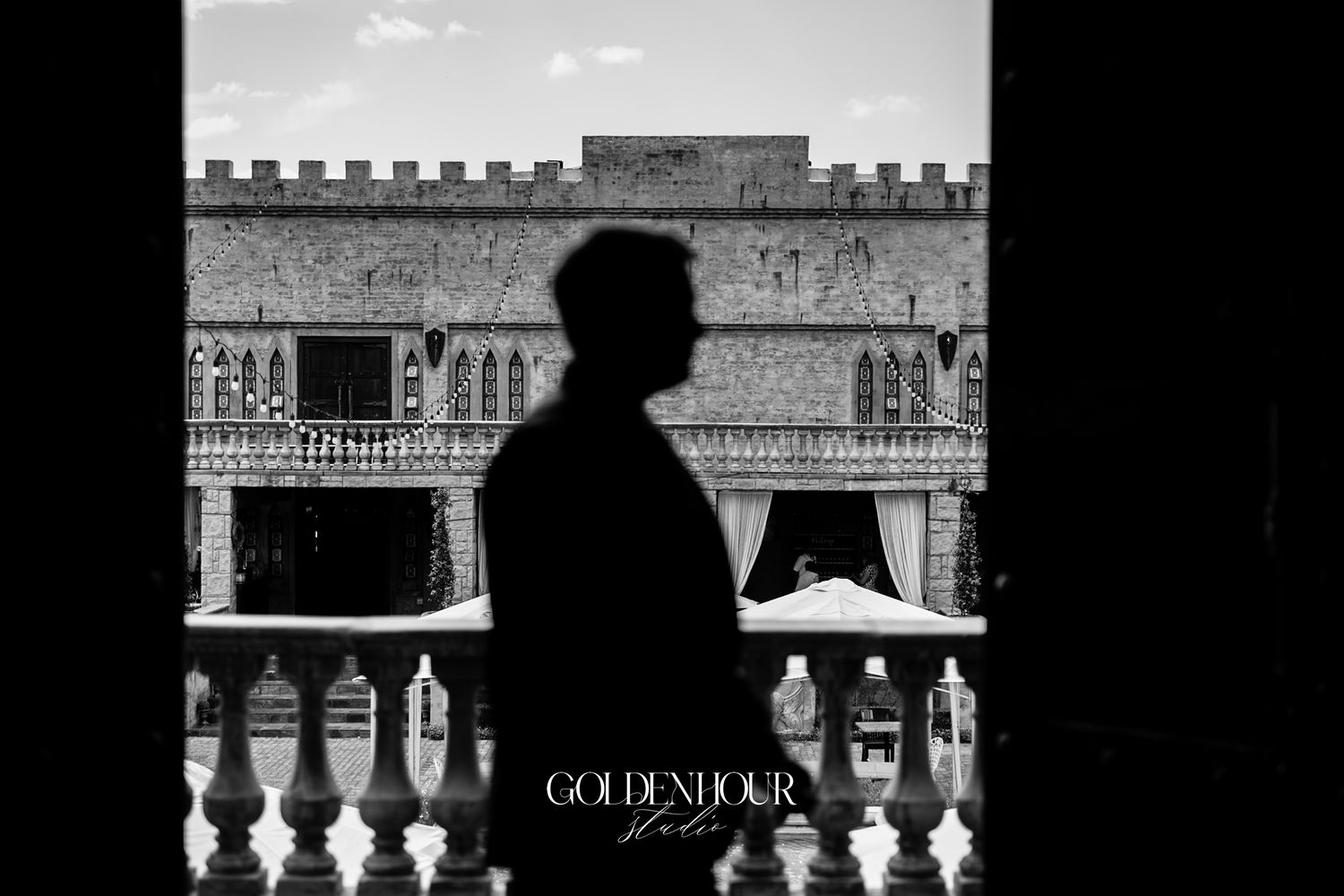 Black and white silhouette of groom standing before ornate wedding venue facade.
