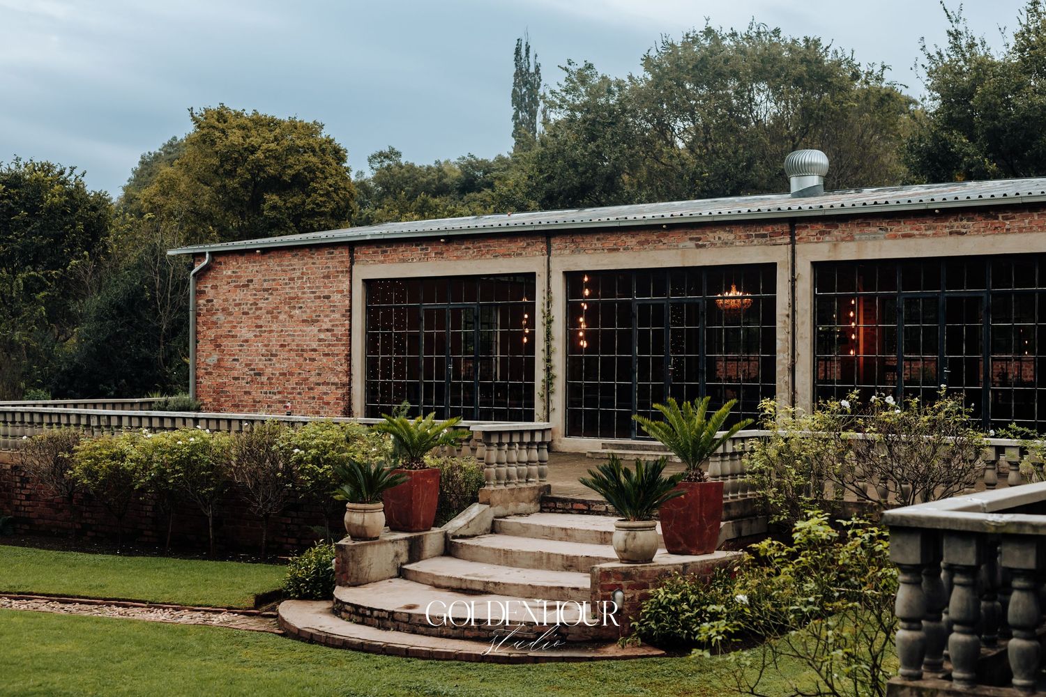 Charming brick wedding venue with manicured gardens, stone steps, and warm string lights inside.