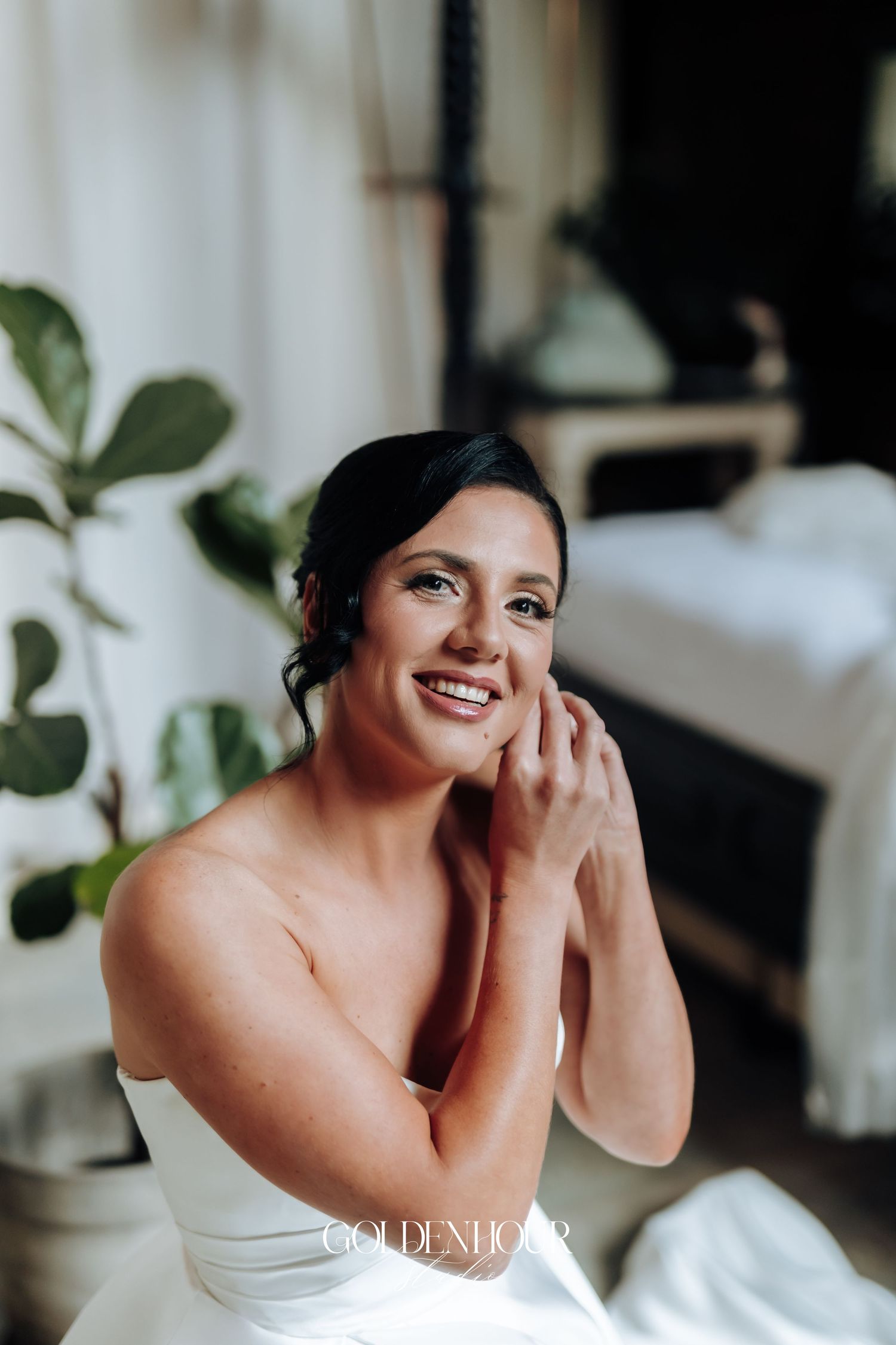 Beautiful dark-haired bride in strapless white gown smiling warmly during wedding morning preparations.