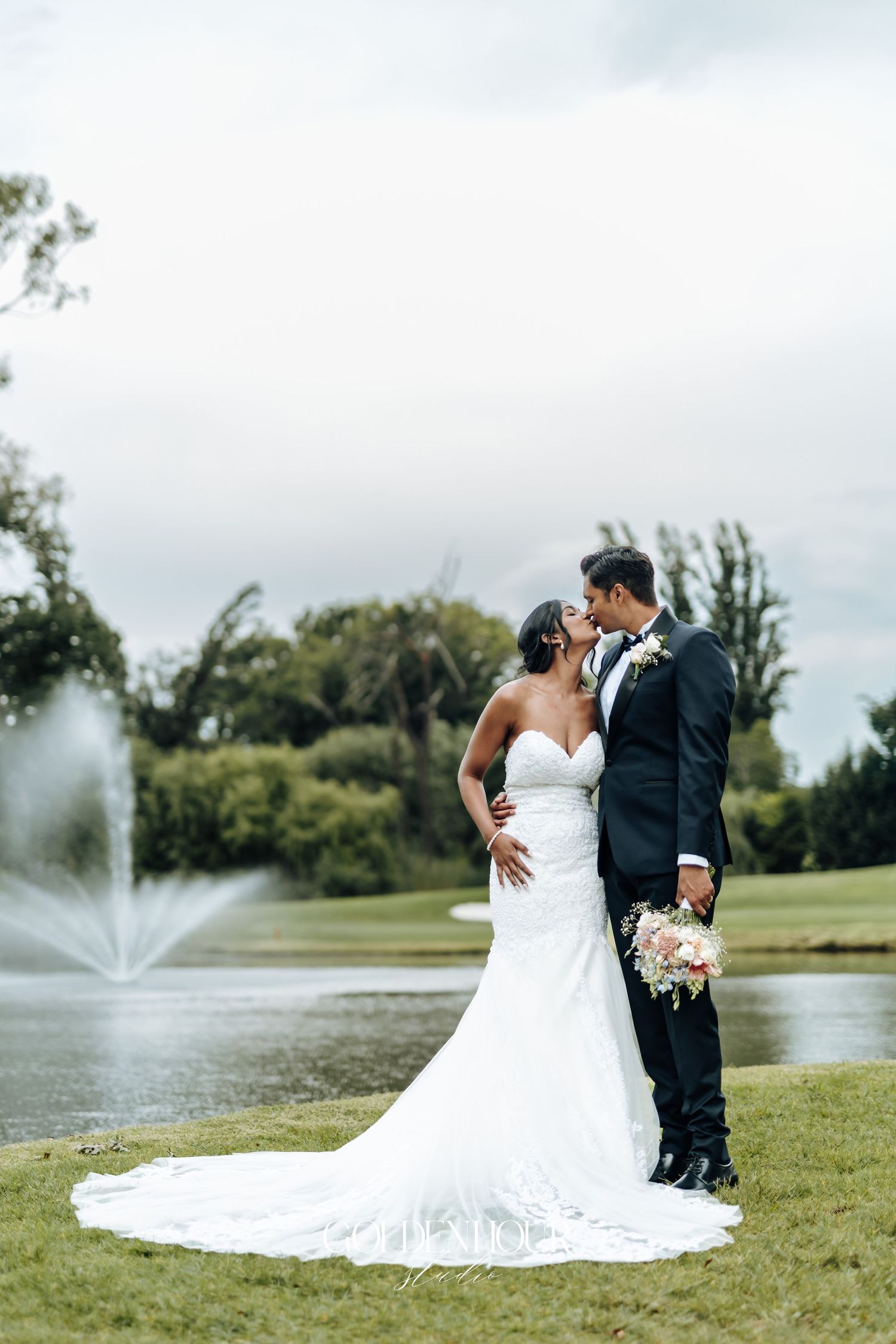 Wedding couple embracing by a fountain on a manicured golf course.