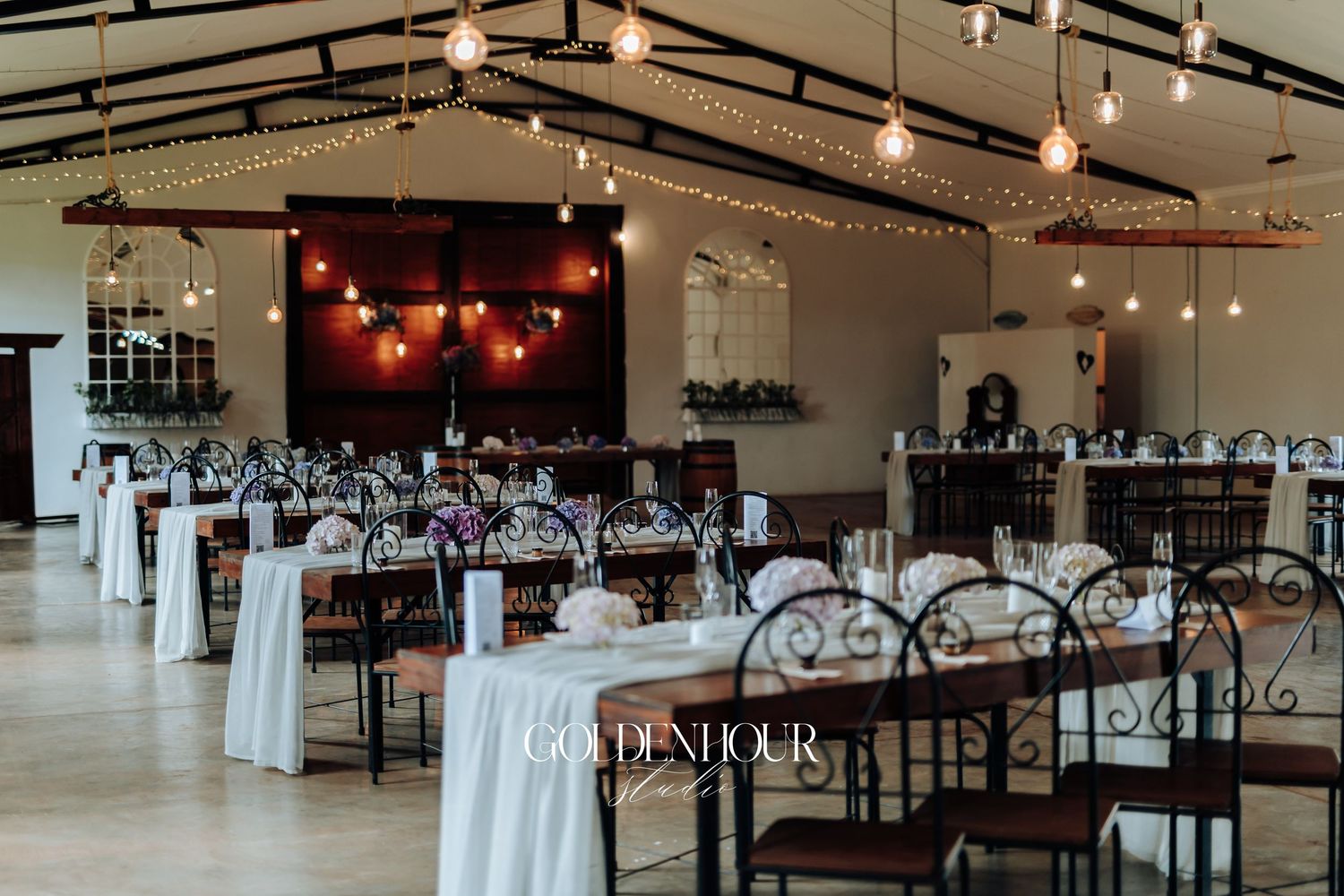 Modern banquet hall with track lighting, dark wood tables, and white draping for an elegant event setup.