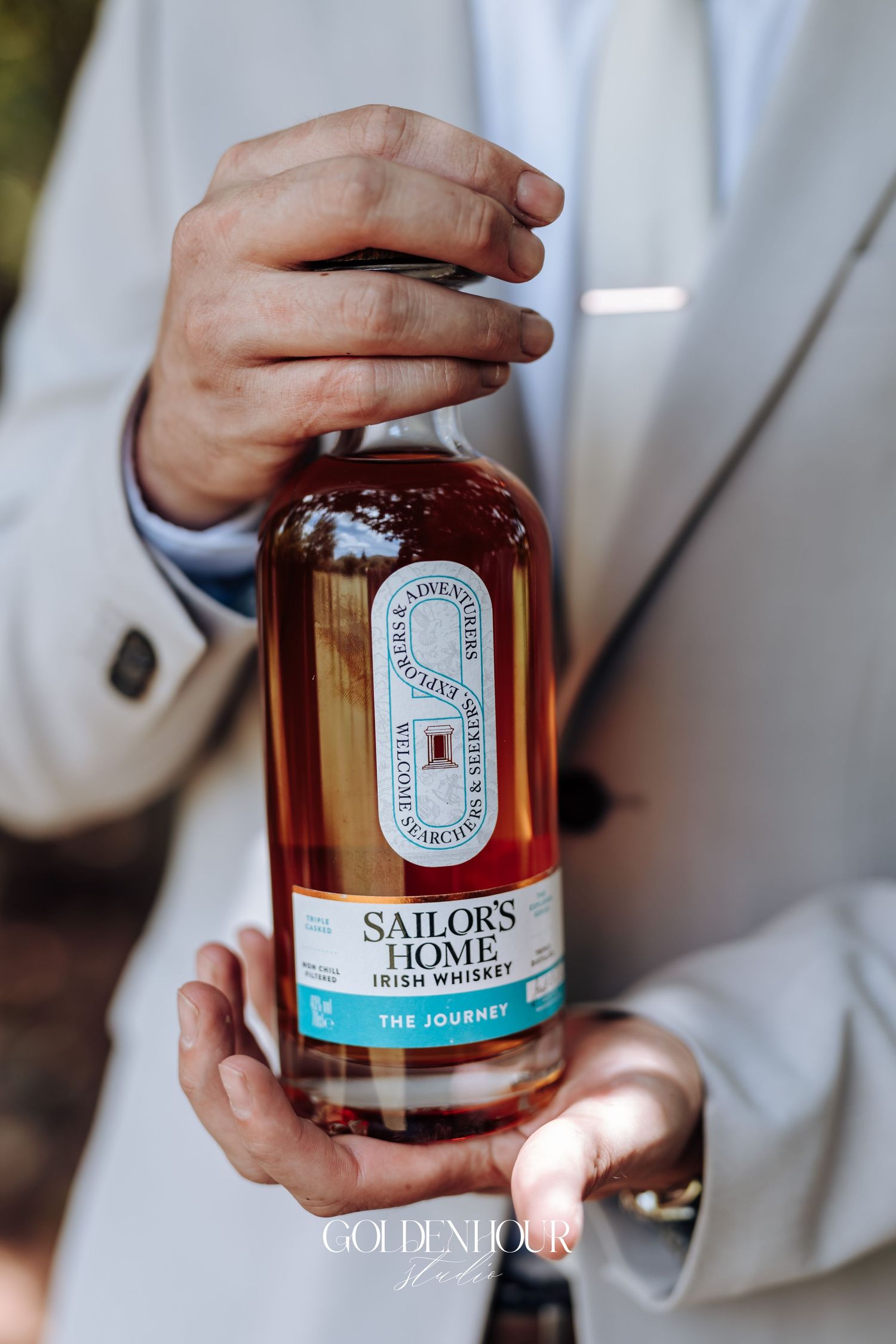 Hands holding a bottle of Sailors Home Irish whiskey against a white suit background.