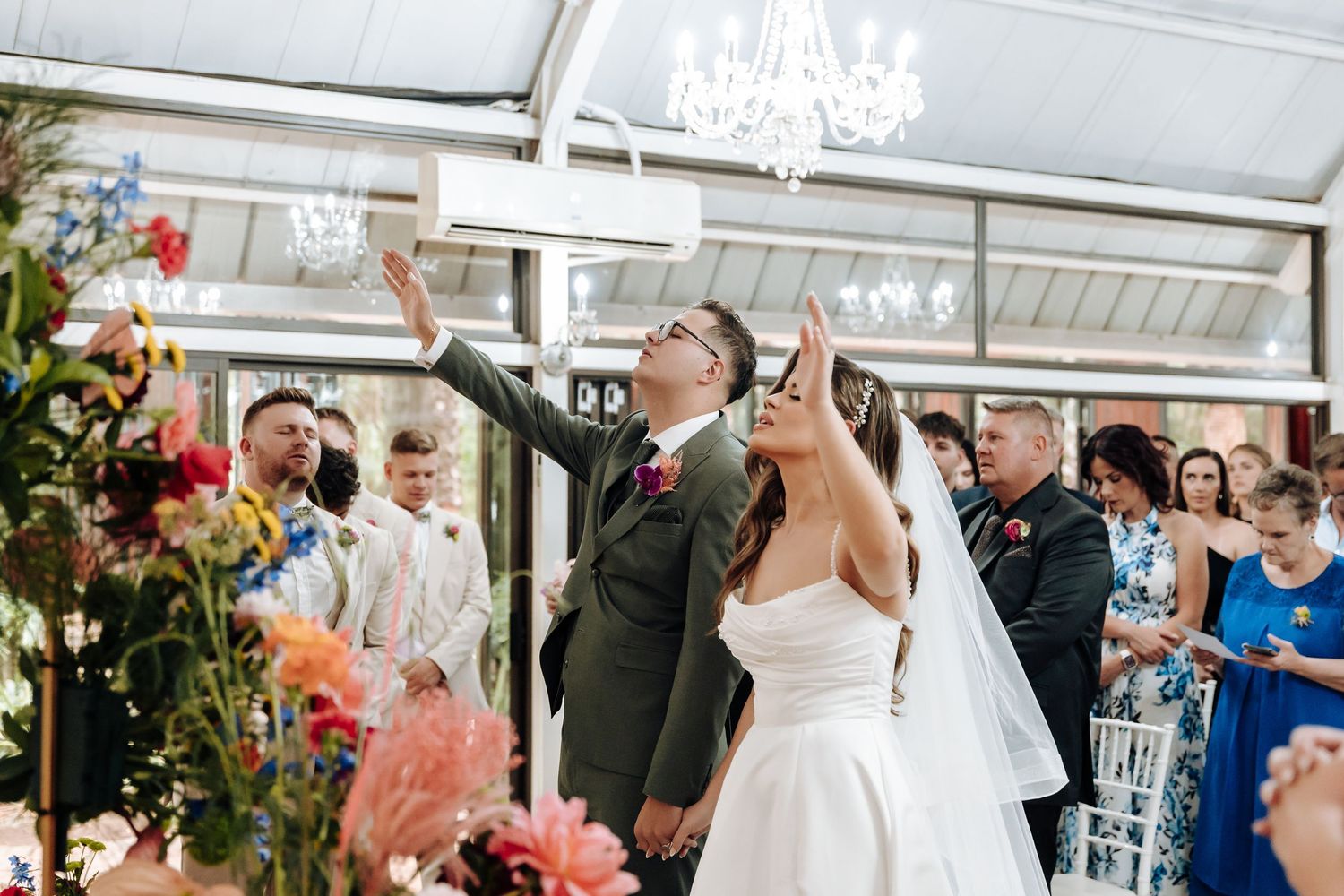 Wedding celebration scene with guests throwing confetti in a sunlit reception hall.