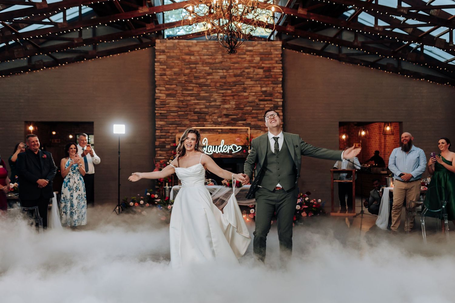 Newlyweds dance on a misty dancefloor in an elegant indoor reception venue with exposed beams.