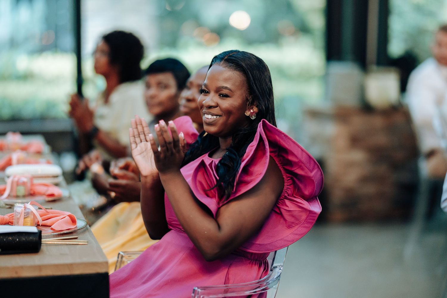 Wedding guest in bright pink dress clapping and smiling during reception celebration.