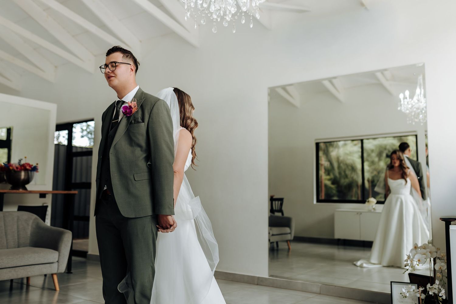 Wedding party poses together in an elegant white room with crystal chandelier and modern decor.