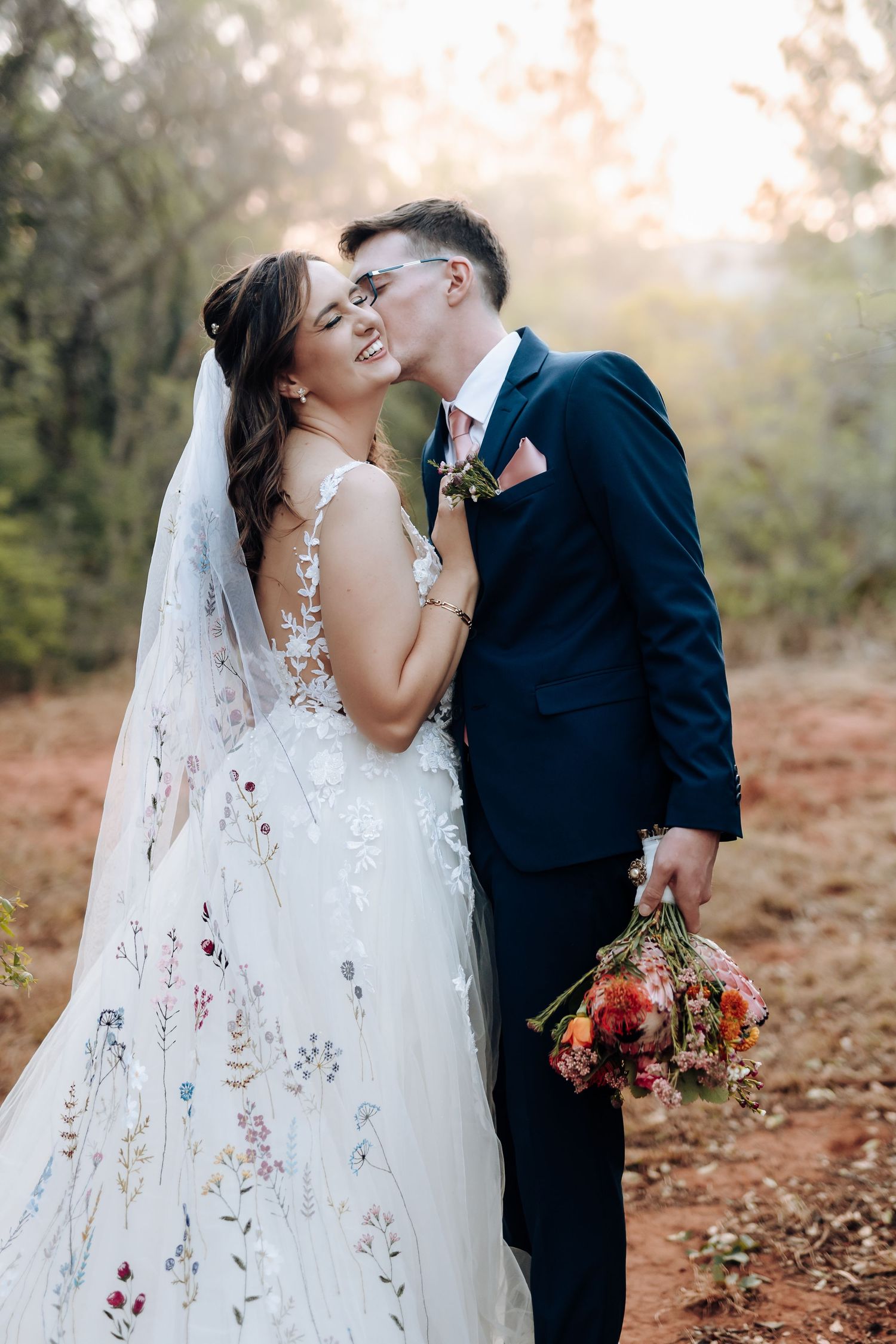 A romantic wedding couple shares intimate moments in a rustic autumn forest setting with a flowing white veil.