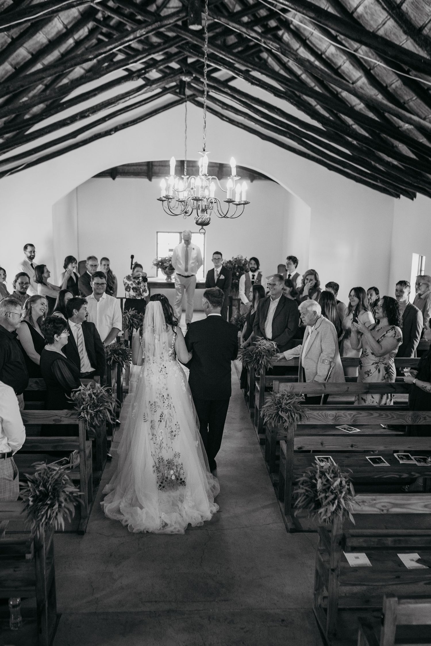 A wedding ceremony procession walking down the aisle of a rustic wooden church with exposed beams and pews.