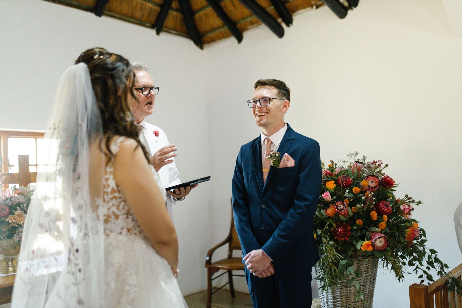 A wedding couple shares joyful moments during their ceremony in a rustic venue with exposed wooden beams.