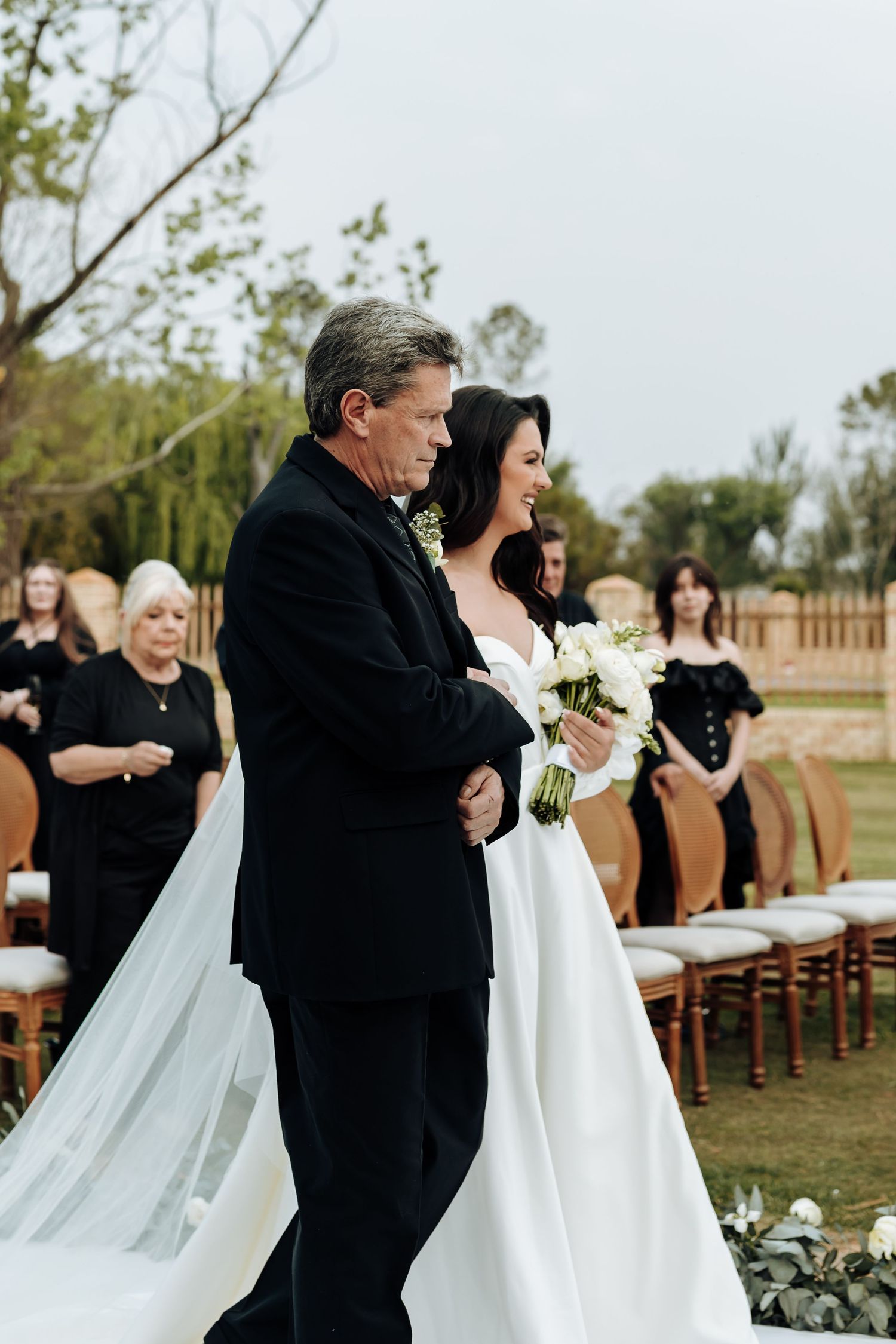 Outdoor wedding ceremony with wooden chairs and floral decorations on a grassy lawn.