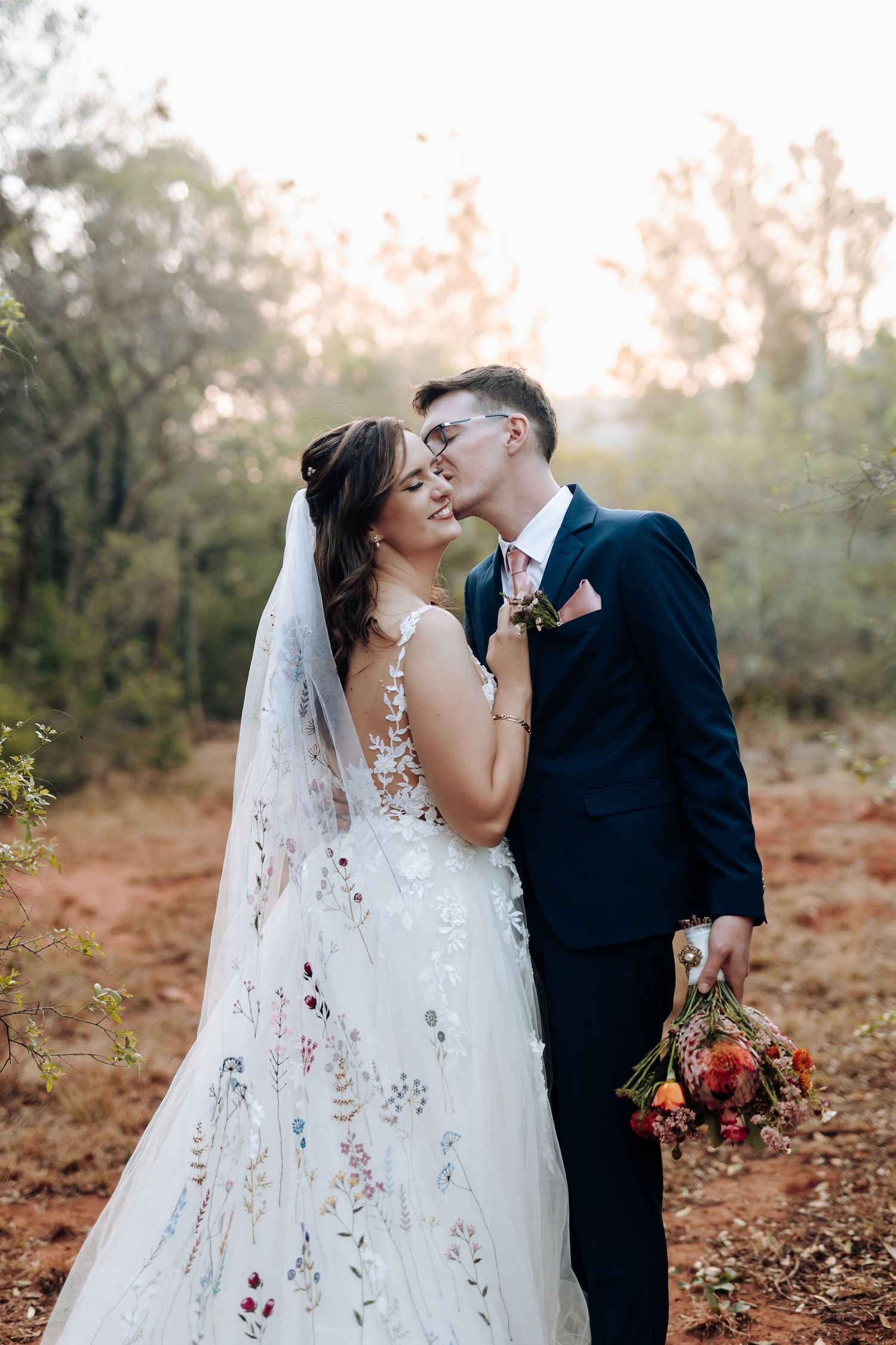 A romantic wedding couple shares intimate moments in a rustic outdoor setting during golden hour.