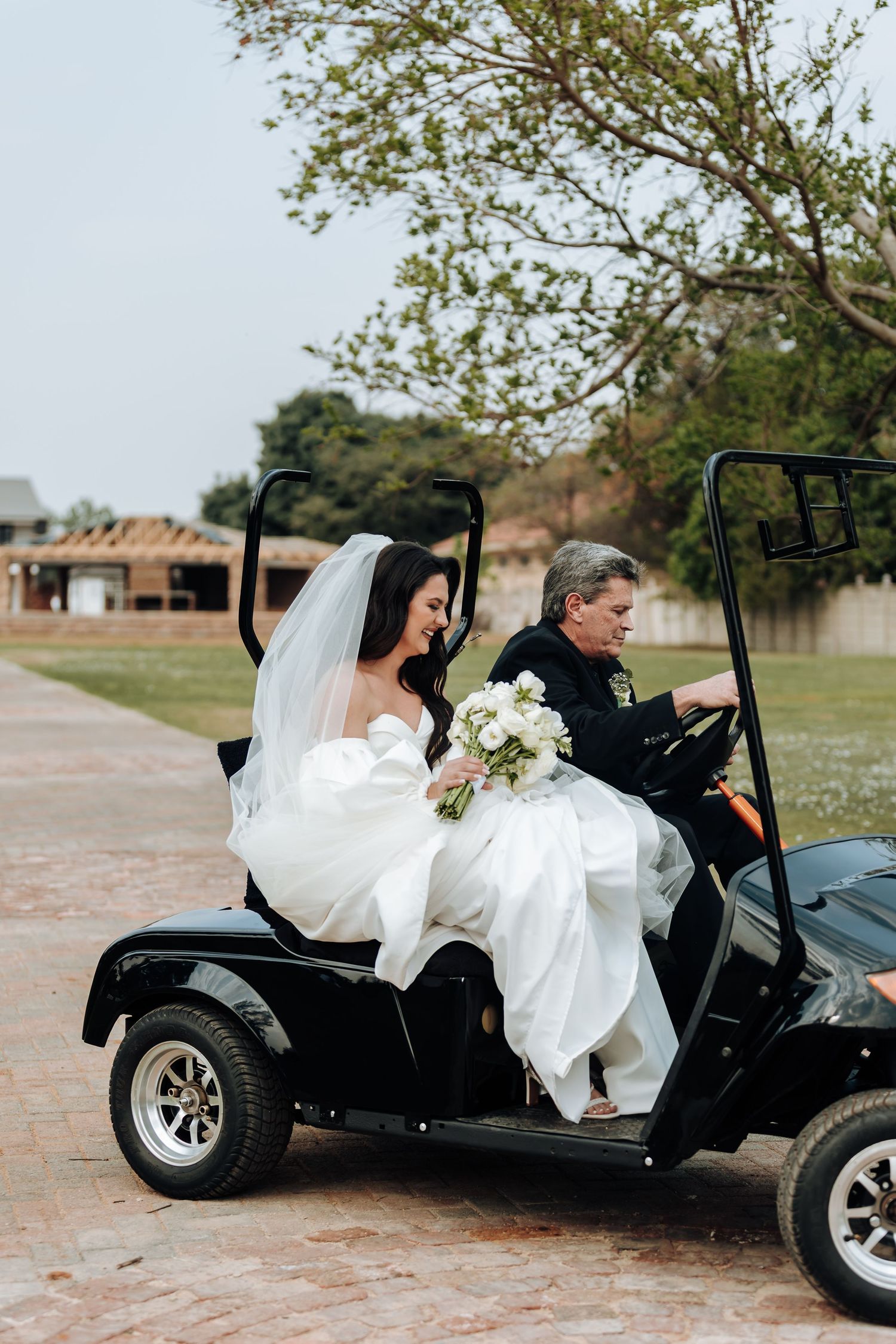 A bride in a flowing white wedding dress getting into a black dune buggy vehicle at an outdoor venue.