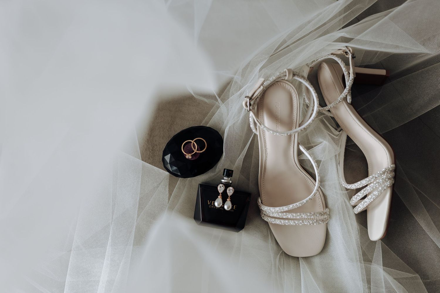 Wedding rings and elegant bridal shoes arranged artistically on white fabric for a romantic detail shot.