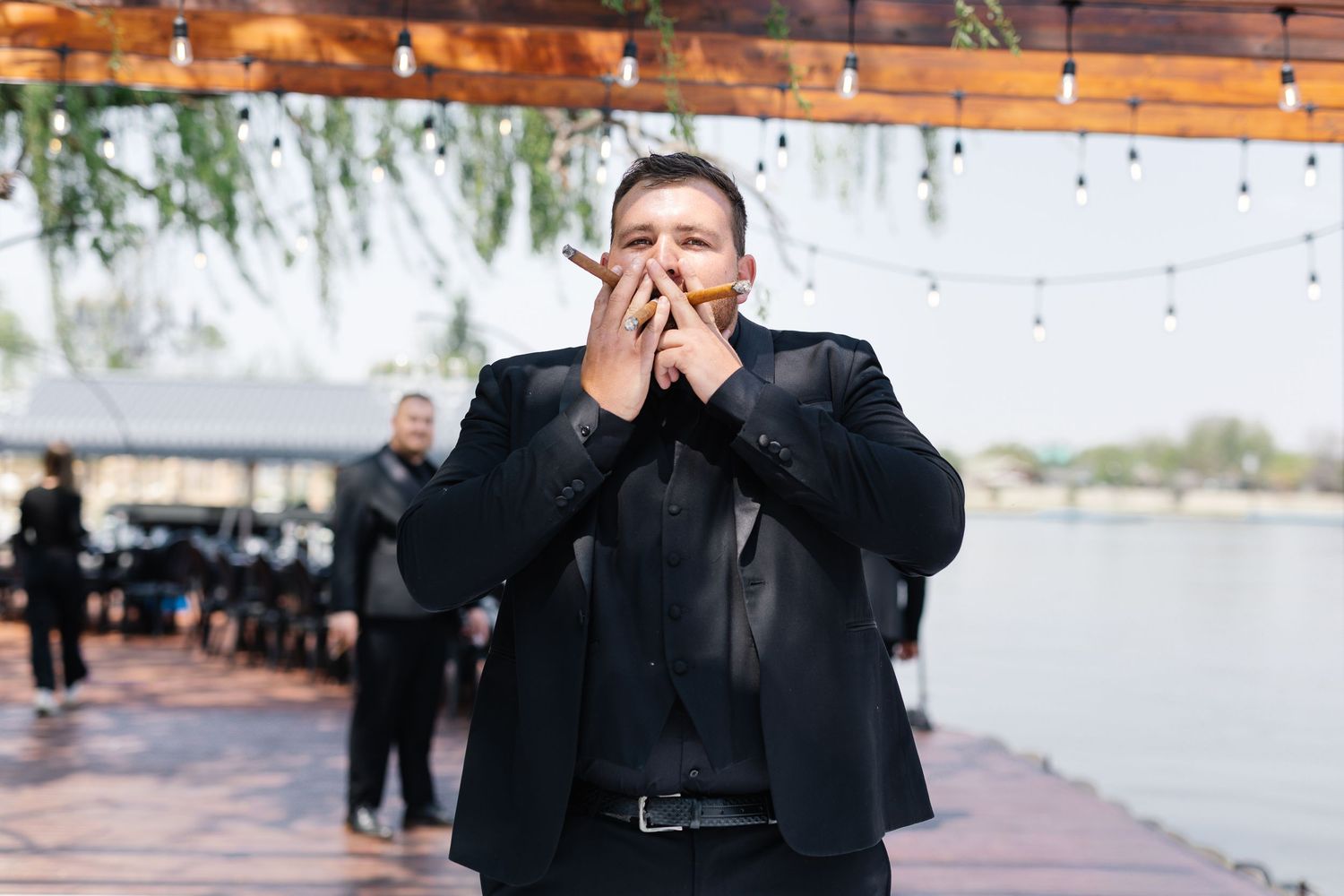 A group of people in formal attire dance and celebrate at an outdoor waterfront venue during sunset.