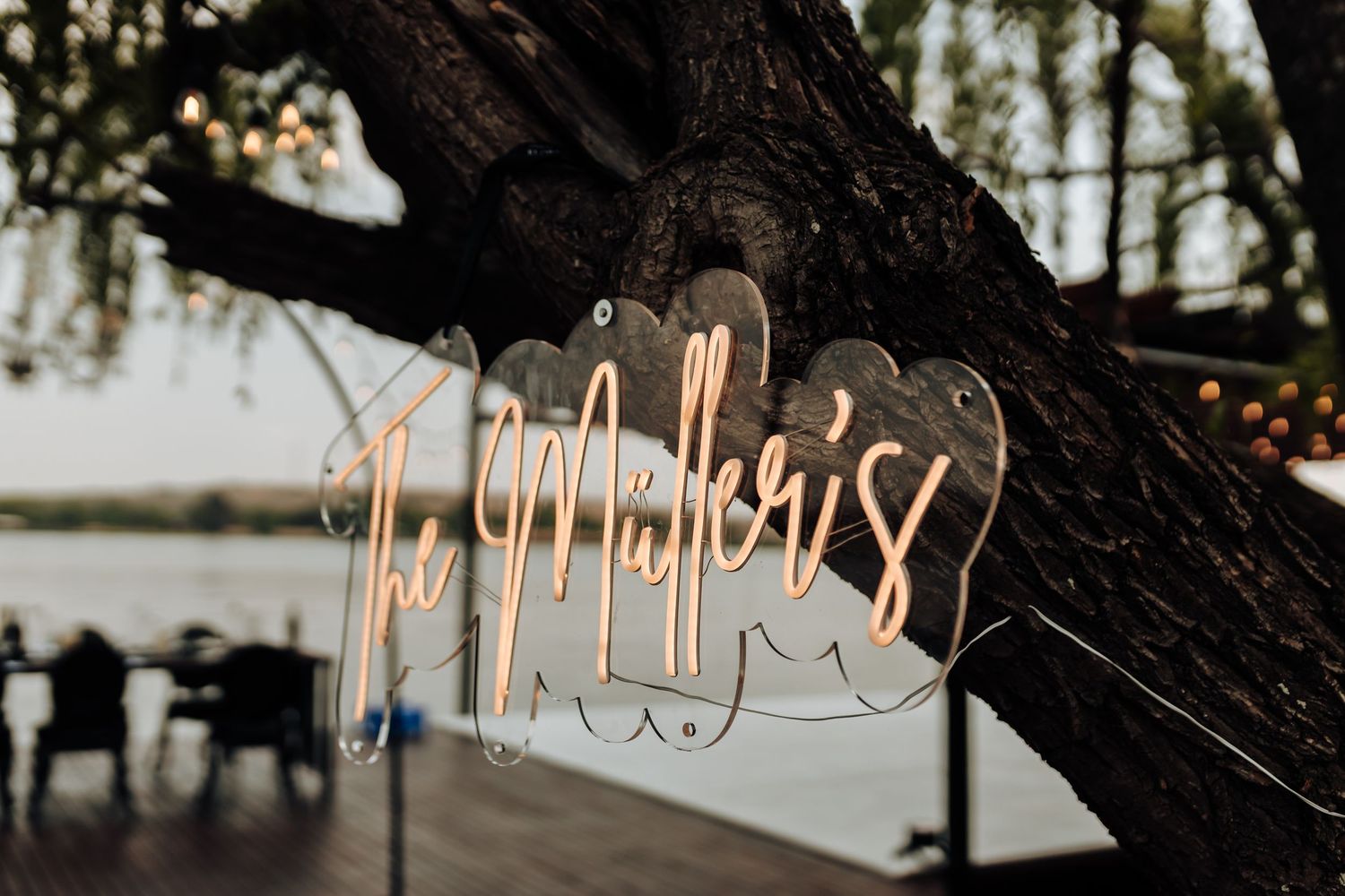 Neon sign with cursive text glows warmly against a dark background with trees silhouetted at dusk.