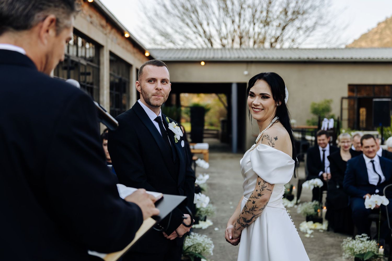 A couple stands before an officiant during an outdoor wedding ceremony with guests in attendance.
