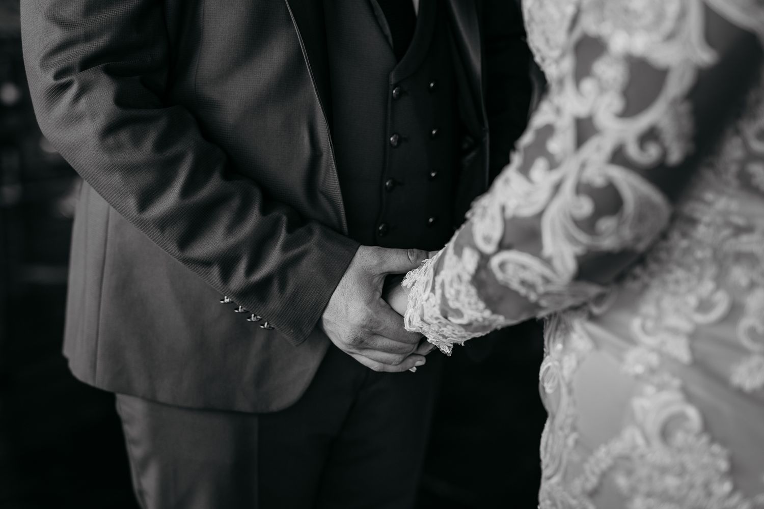 Black and white close-up of couple holding hands during wedding ceremony.